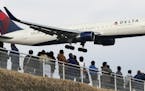 FILE - In this March 14, 2015 file photo, people watch a landing Delta Air Lines jet approach the Narita International Airport from a popular viewing 