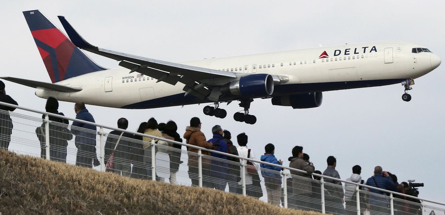 FILE - In this March 14, 2015 file photo, people watch a landing Delta Air Lines jet approach the Narita International Airport from a popular viewing spot at Sakuranoyama Park in Narita, east of Tokyo.