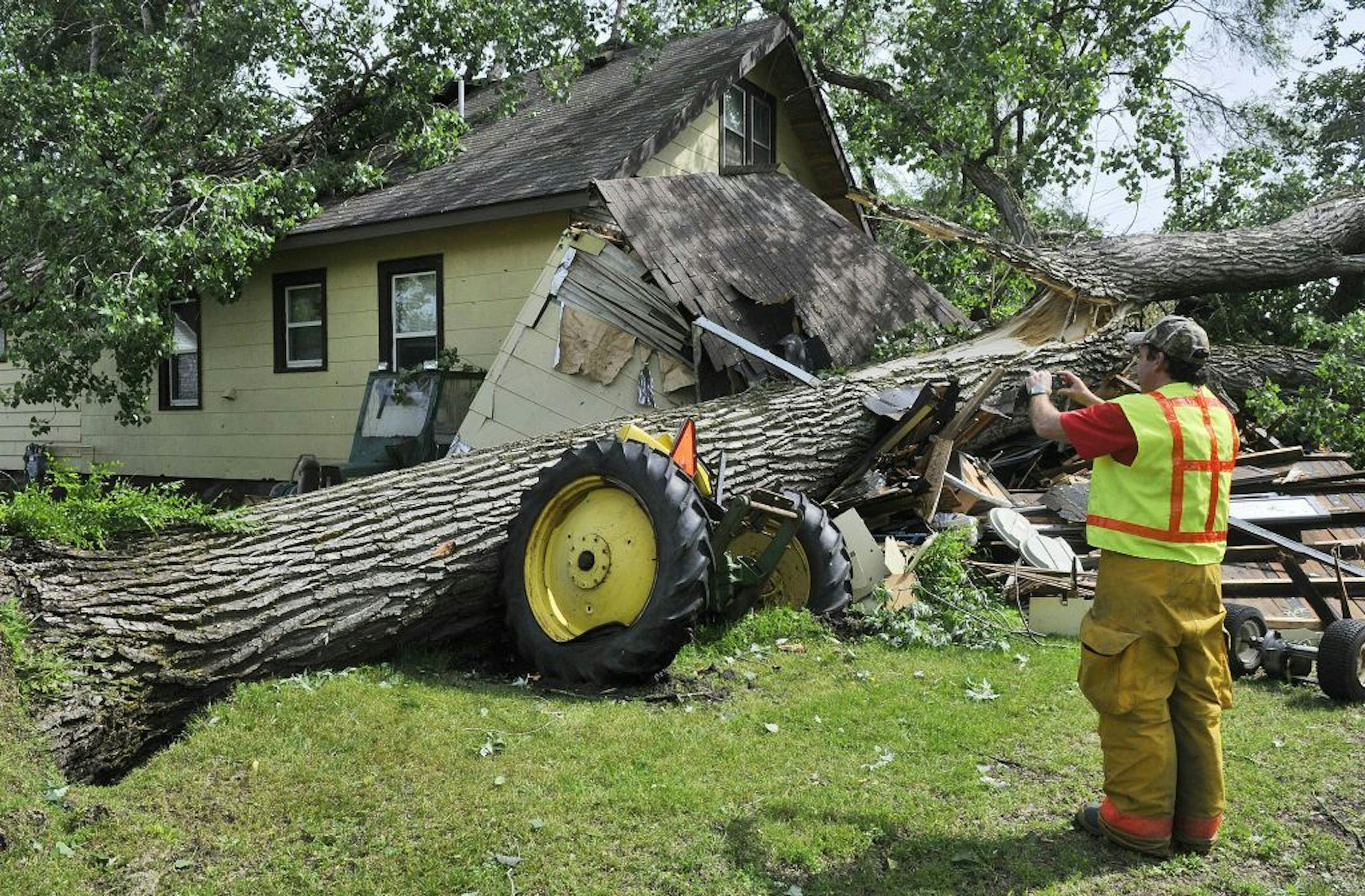 ADVANCE FOR MONDAY, SEPT 9 - FILE - In this June 21, 2013 file photo, Fire Chief Rodney Schaefer stops to take a photo of a downed tree on a home and antique tractor in Rockville, Minn. after a strong overnight storm caused damage over much of central Minnesota. Minnesota legislative leaders will hold a special session on Sept. 9 to provide relief to Minnesota areas hit hard by June 2013 storms. Two lawmakers argue that the expense of such special sessions could be defrayed with the creation of