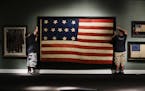 In this Wednesday, June 12, 2019 photo, workmen hang a Federal Era flag as part of the new exhibit "A New Constellation: A Collection of Historic 13-S
