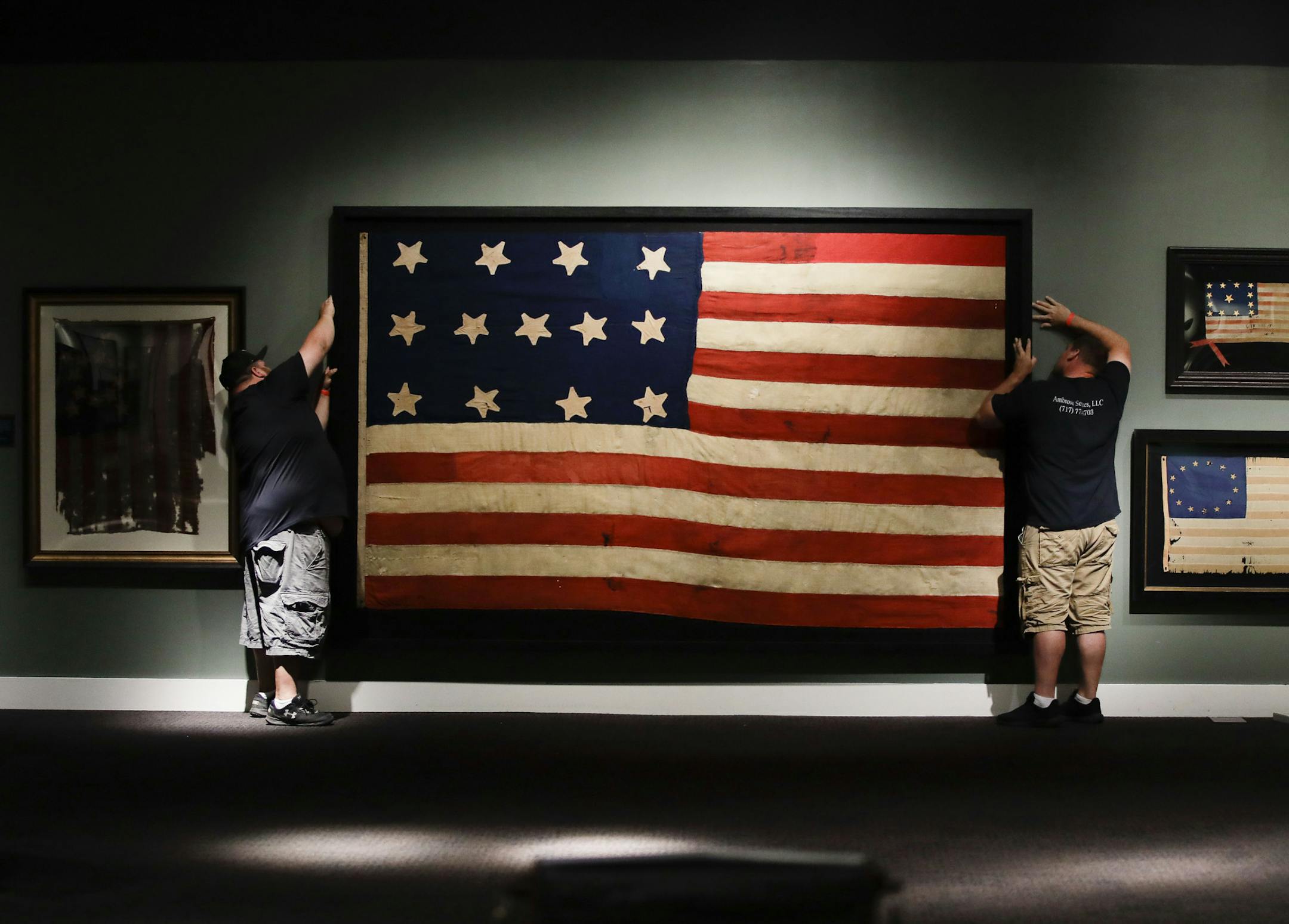 In this Wednesday, June 12, 2019 photo, workmen hang a Federal Era flag as part of the new exhibit "A New Constellation: A Collection of Historic 13-Star Flags," at the Museum of the American Revolution in Philadelphia. The exhibit featuring 40 rare, historic 13-star flags is scheduled to run from Flag Day, Friday, June 14 through Sunday, July 14. (AP Photo/Matt Rourke)