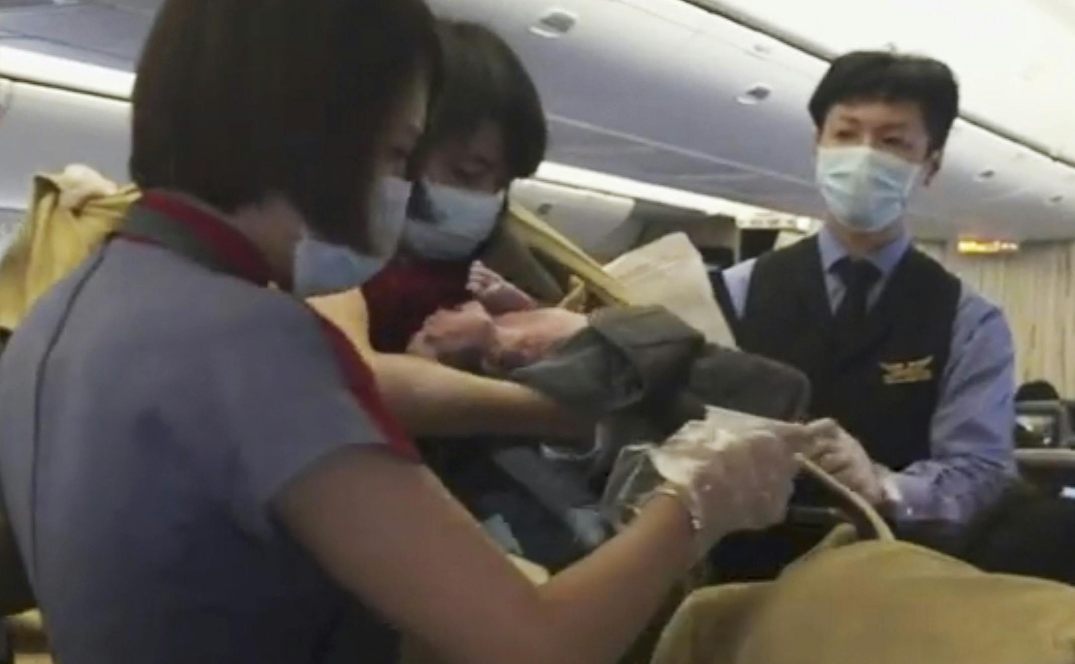 In an image from AP video, a member of the plane's crew holds up a newborn after Dr. Angelica Zen, who is obscured at lower right, delivered the baby on a China Air flight from Taiwan on Oct. 7, 2015. A passenger had gone into labor, and the flight was diverted to Alaska. Mother and newborn daughter left for a hospital, and the flight continued on to Los Angeles. (Edmund Chen/AP Video via AP Photo)