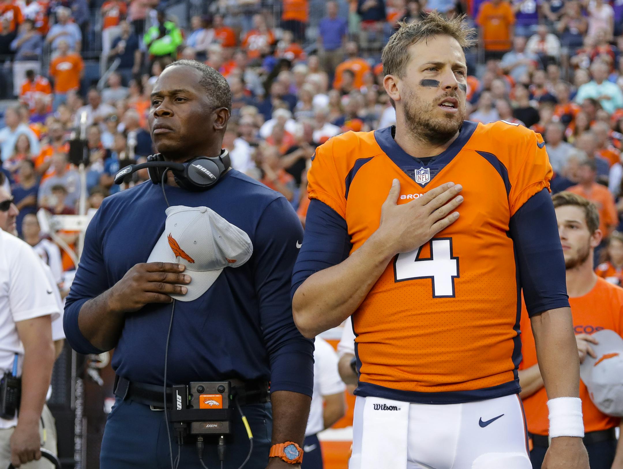FILE - In this Aug. 11, 2018, file photo, Denver Broncos quarterback Case Keenum and Vance Joseph hold their hands over their hearts during the national anthem before an NFL football game against the Minnesota Viking in Denver. When things go sour, an NFL team's fan base often points to two people: the guy calling plays on the sideline, and the man behind center trying to execute them. (AP Photo/Jack Dempsey, FIle) ORG XMIT: NYDD203