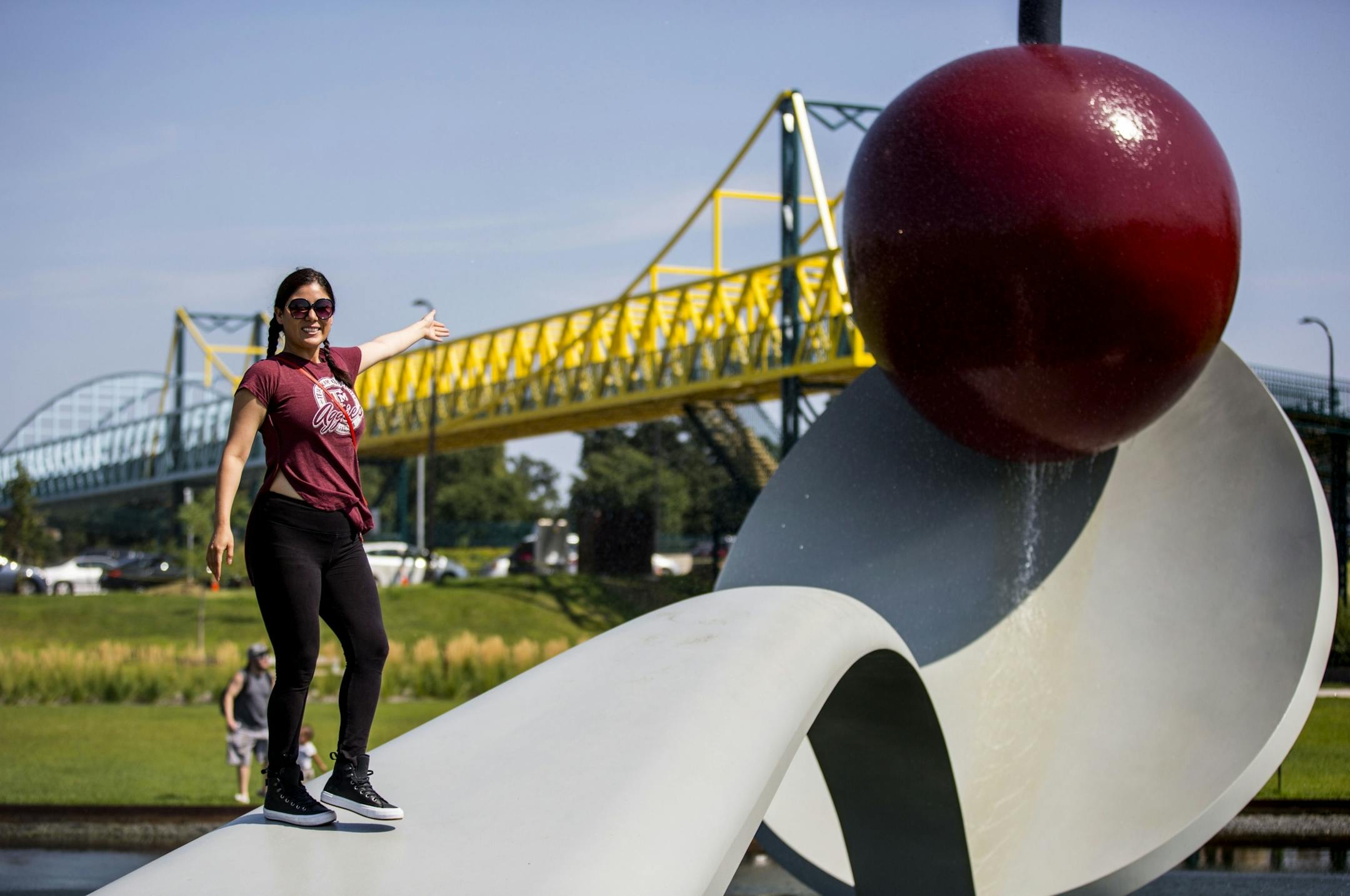 Beatrice Guerrero poses for a photo on the famous spoon and cherry sculpture as the bridge cuts across the sky in the background.