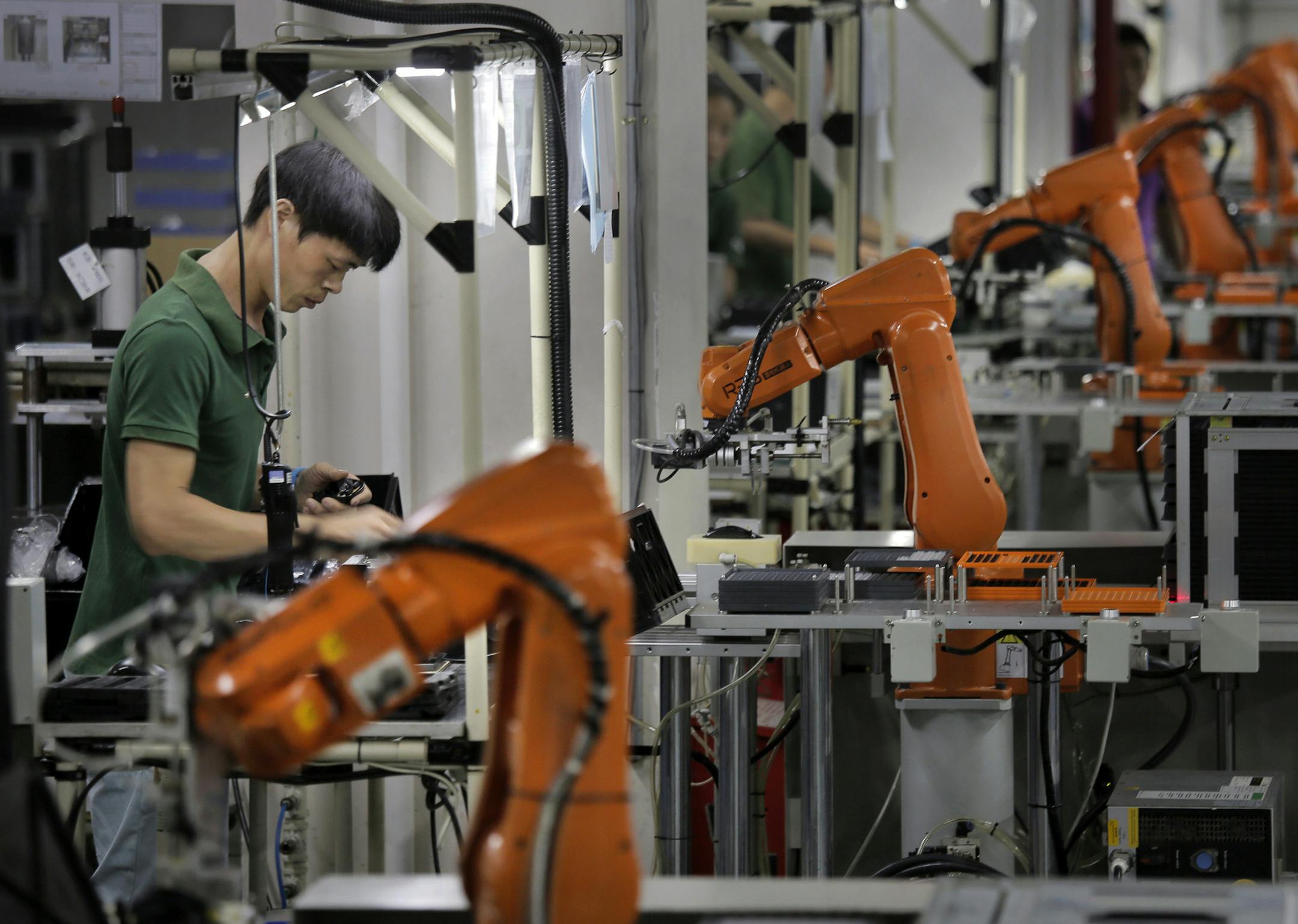 In this Aug. 21, 2015 photo, a Chinese man works amid orange robot arms at Rapoo Technology factory in southern Chinese industrial boomtown of Shenzhen. Factories in China are rapidly replacing those workers with automation, a pivot thatís encouraged by rising wages and new official directives aimed at helping the country move away from low-cost manufacturing as the supply of young, pliant workers shrinks. (AP Photo/Vincent Yu)