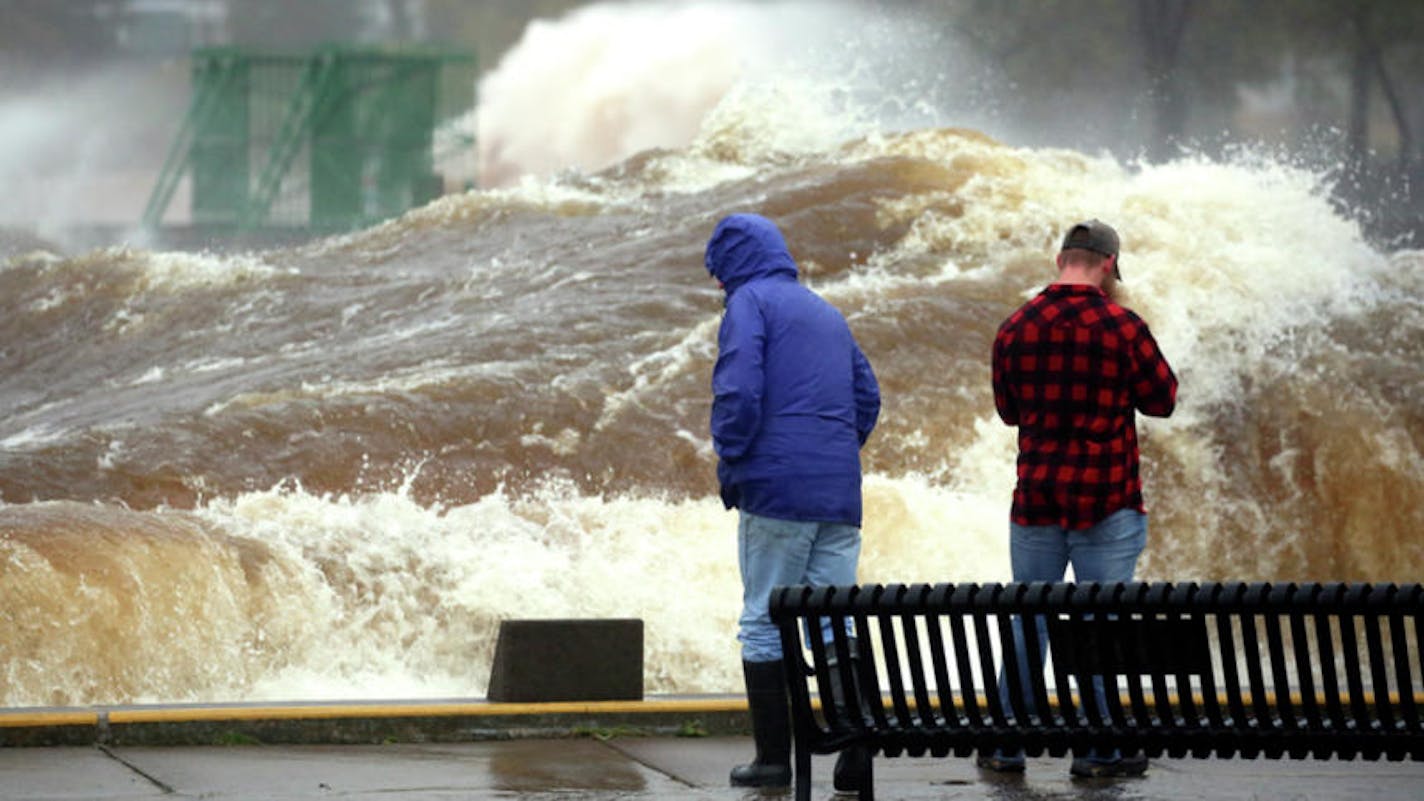 A large wave rolls past two spectators and down the length of the Duluth Ship Canal on Wednesday morning. (Steve Kuchera / Duluth News Tribune)