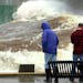 A large wave rolls past two spectators and down the length of the Duluth Ship Canal on Wednesday morning. (Steve Kuchera / Duluth News Tribune)