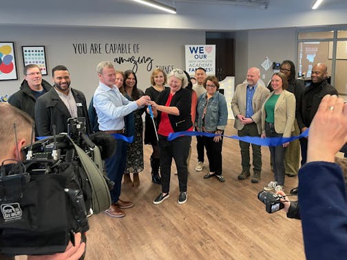 Chad Dunkley, CEO of New Horizons Academy, and Jean Deshler, mayor of Crystal, cut a ceremonial ribbon for the opening of a new child care center in Crystal on Feb. 3, 2025. Members of the Crystal city council, state legislators and other state officials surround them.