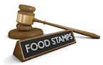 Government assistance concept of a wooden court gavel lying next to a sign that reads food stamps, rendered in 3D over a white background.