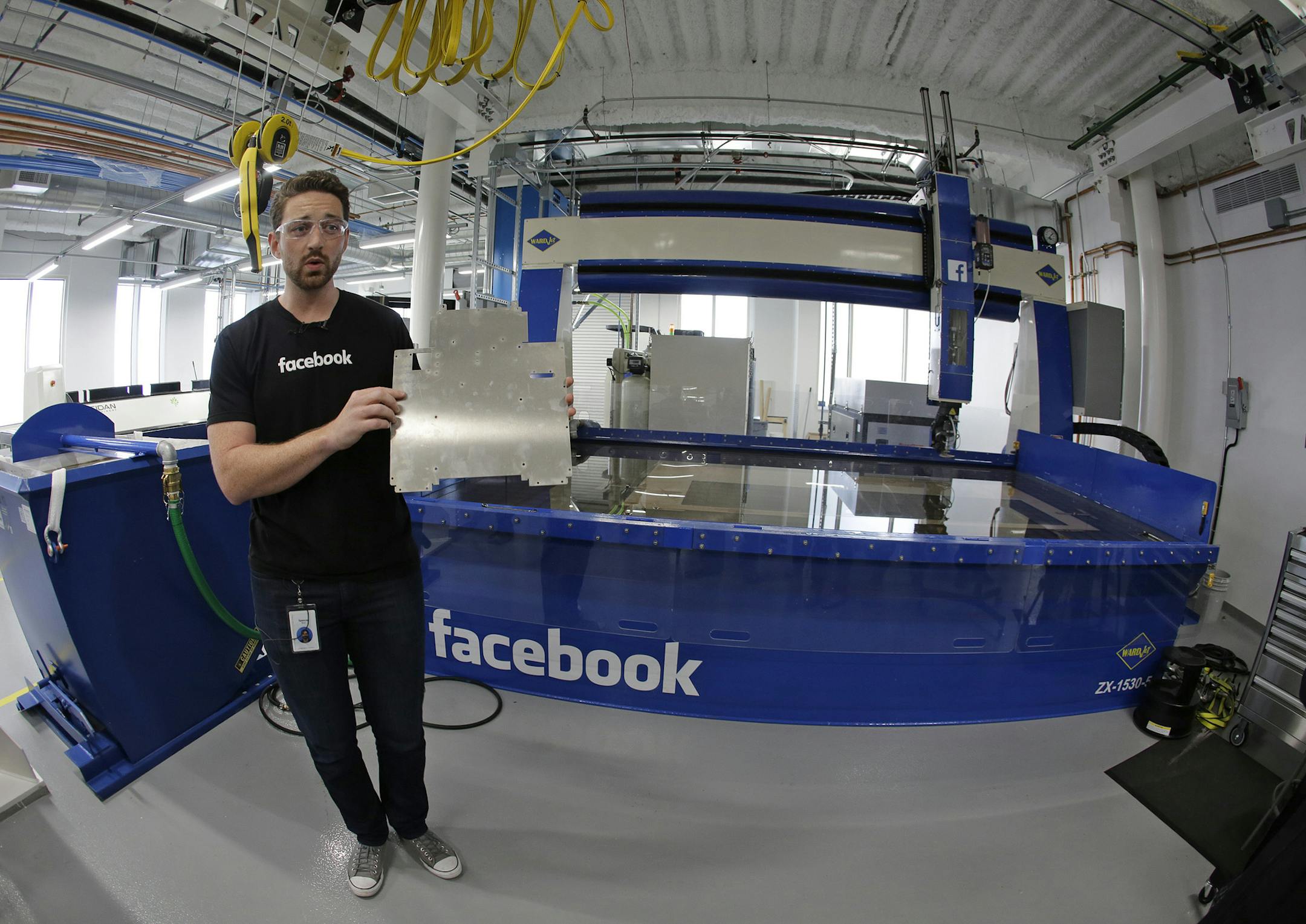 In this photo taken Tuesday, Aug. 2, 2016, model maker Spencer Burns, holds up a piece of sheet metal while standing in front of a water jet during a tour of Area 404, the hardware R&D lab, at Facebook headquarters in Menlo Park, Calif. (AP Photo/Eric Risberg)