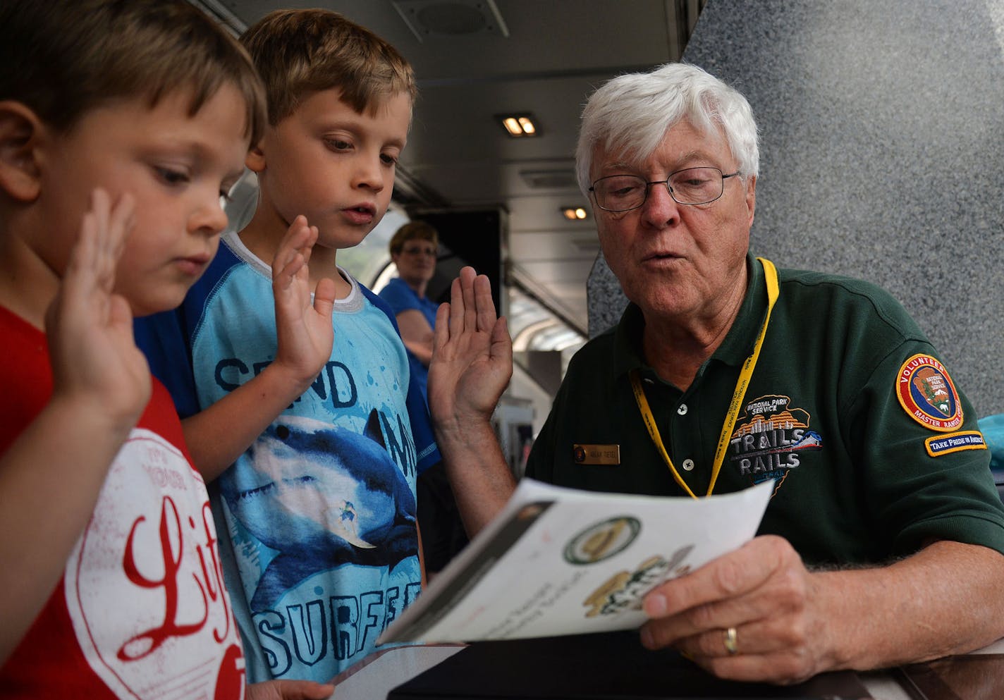 From left, brothers Raymond, 6, and Steven, 8, Hladovcak, both of Illinois, raised their hands to recite the oath to become Junior Rangers, inducted by Volunteer Master Ranger Corps Arlan Tietel, of Woodbury, as part of the Trails and Rails program on the Amtrak Train that departed from Union Depot in St. Paul, Minn. and went to Chicago, Illinois, on Monday July 27, 2015. ] RACHEL WOOLF &#x2211; rachel.woolf@startribune.com