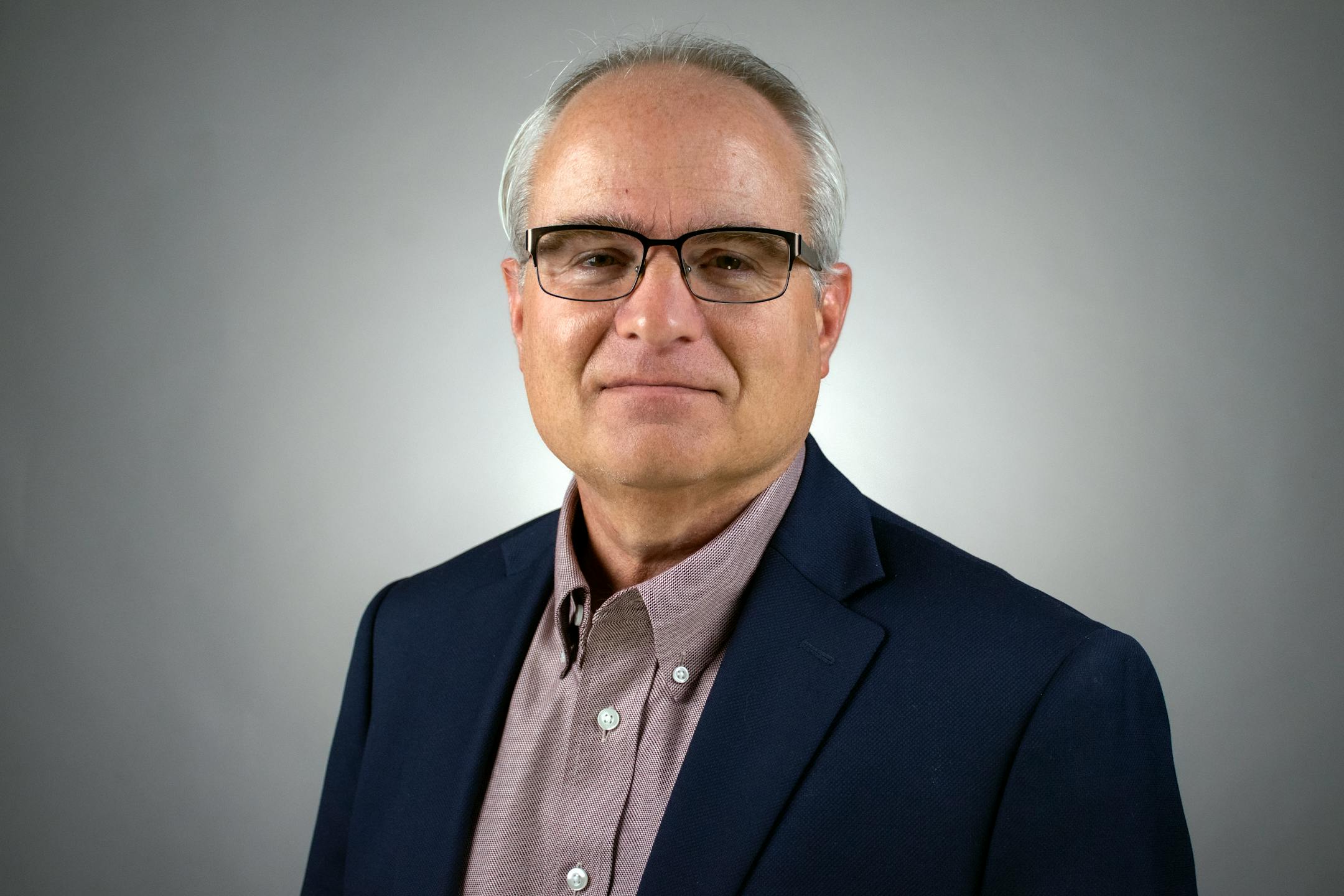 Oklahoma State's Tom Brown wears a suit in front of a gray background. He will serve as the first dean of Bethel University's new school of business.