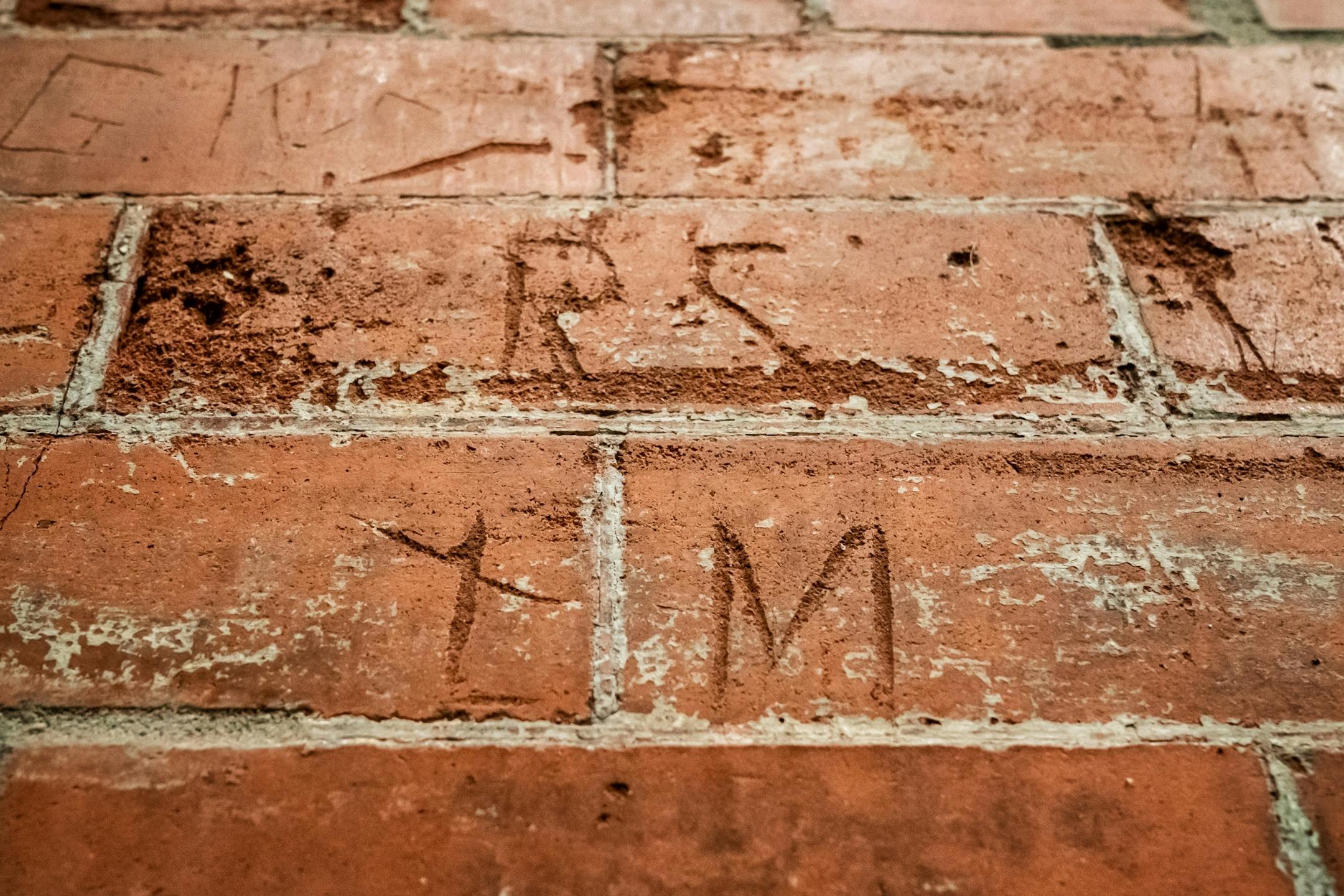 Decades old Initials can be seen carved into brick when it was an open street alley between the Pioneer and Endicott buildings.