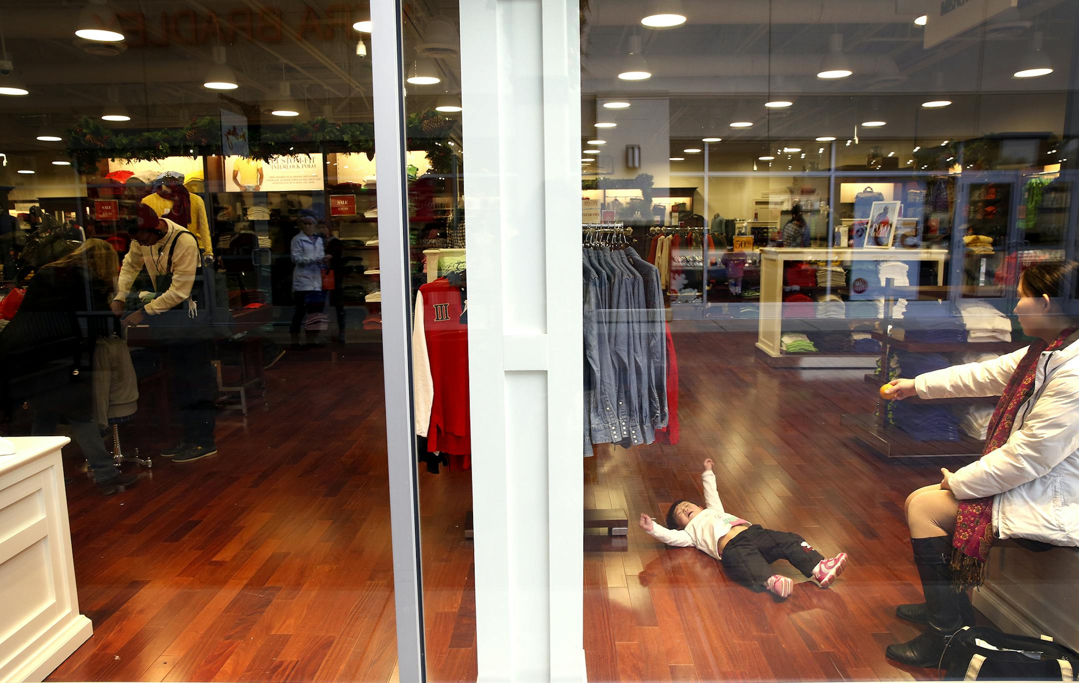 Mindy Bai of Edina tries to placate her daughter Aria Bai, 1 1/2, inside the Polo Ralph Lauren store at Twin Cities Premium Outlets in Eagan on Friday, December 26, 2014. ] LEILA NAVIDI leila.navidi@startribune.com / BACKGROUND INFORMATION: The day after Christmas this year is predicted by ShopperTrak to be the second busiest shopping day of the year, with many people returning unwanted gifts and hunting for bargains.