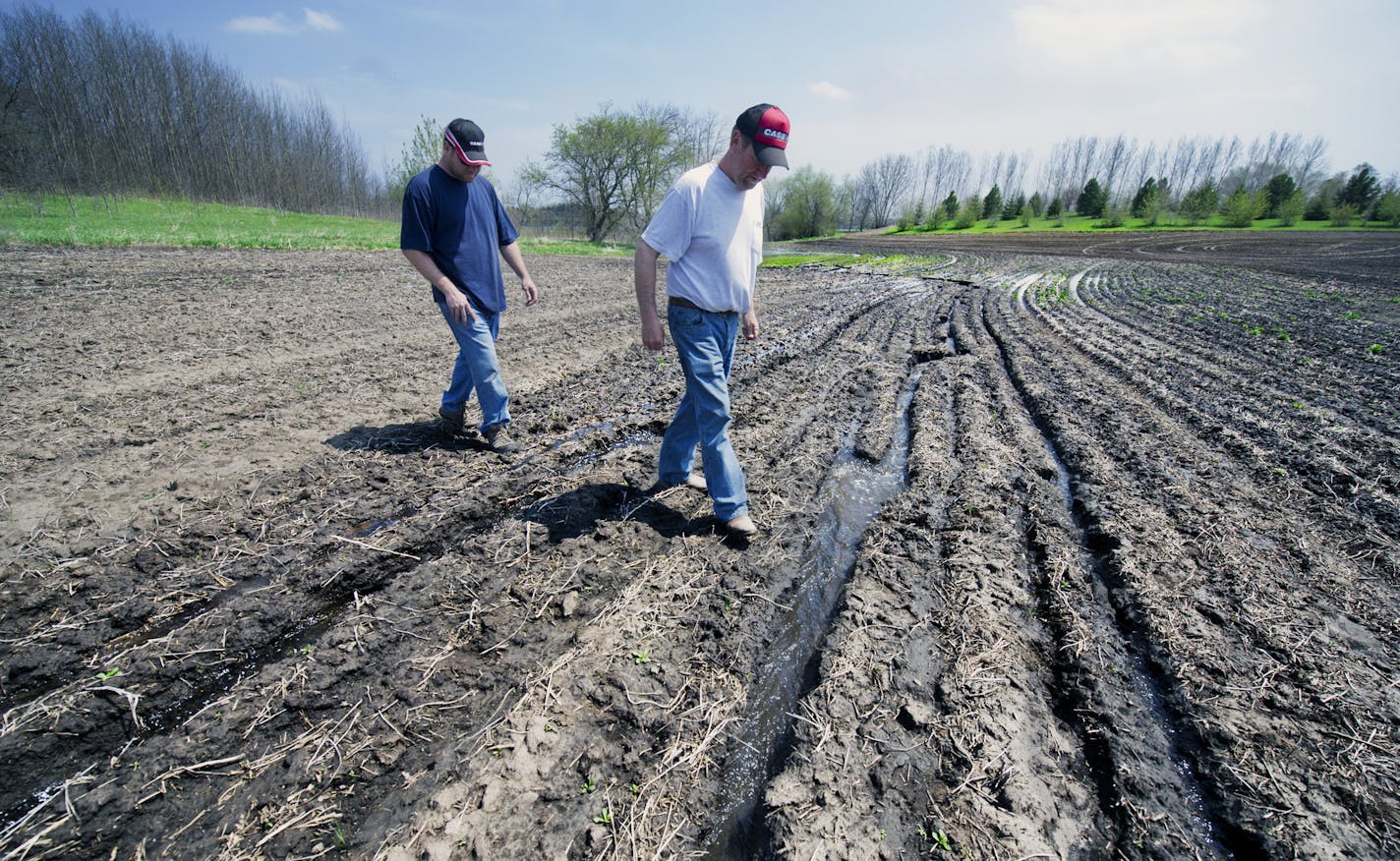 Dave Johnson and his son, Adam, both from the Alexandria area, step over running water in one of their farm fields.