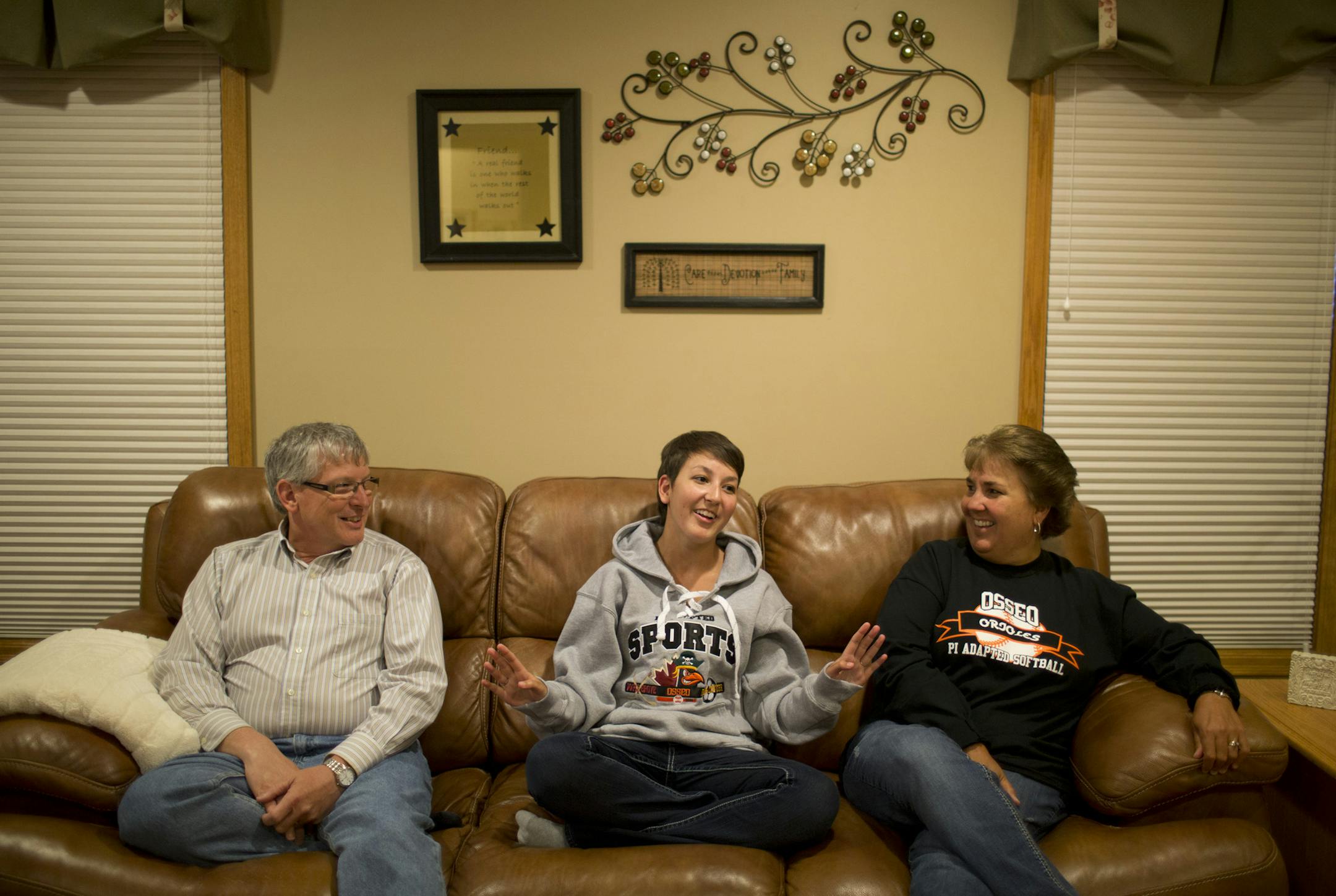 Olivia Maccoux, a Park Center junior who plays adapted softball in the physically impaired division, has worked hard to not let more than 100 surgeries over the course of her life get in the way of achieving her goals in sports or academics. Here she is flanked by her parents, Dan and Cathy Maccoux, in their Brooklyn Park home.