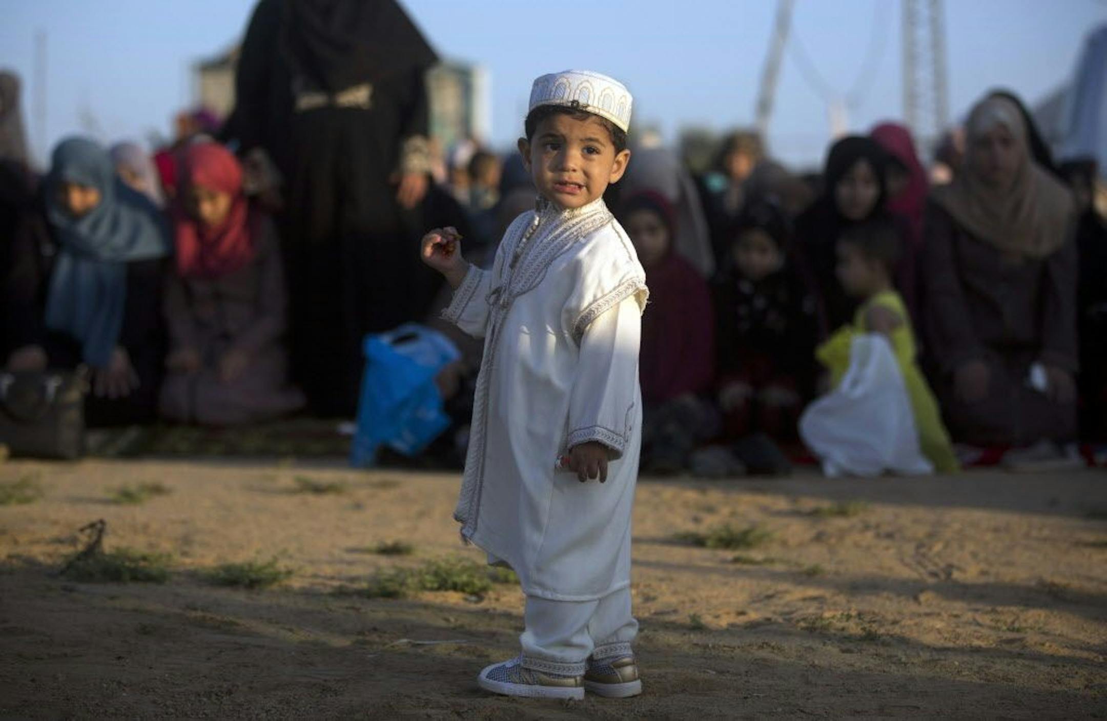 A Palestinian boy wearing a traditional uniform stands in front of Muslim women performing Eid al-Fitr prayers, marking the end of the holy fasting month of Ramadan, in Eastern Gaza City, Friday, June 15, 2018.