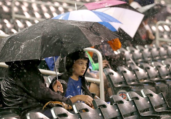 A young Kansas City Royals fan takes cover under an umbrella as a rain delay is called during the third inning of a baseball game between the Royals a