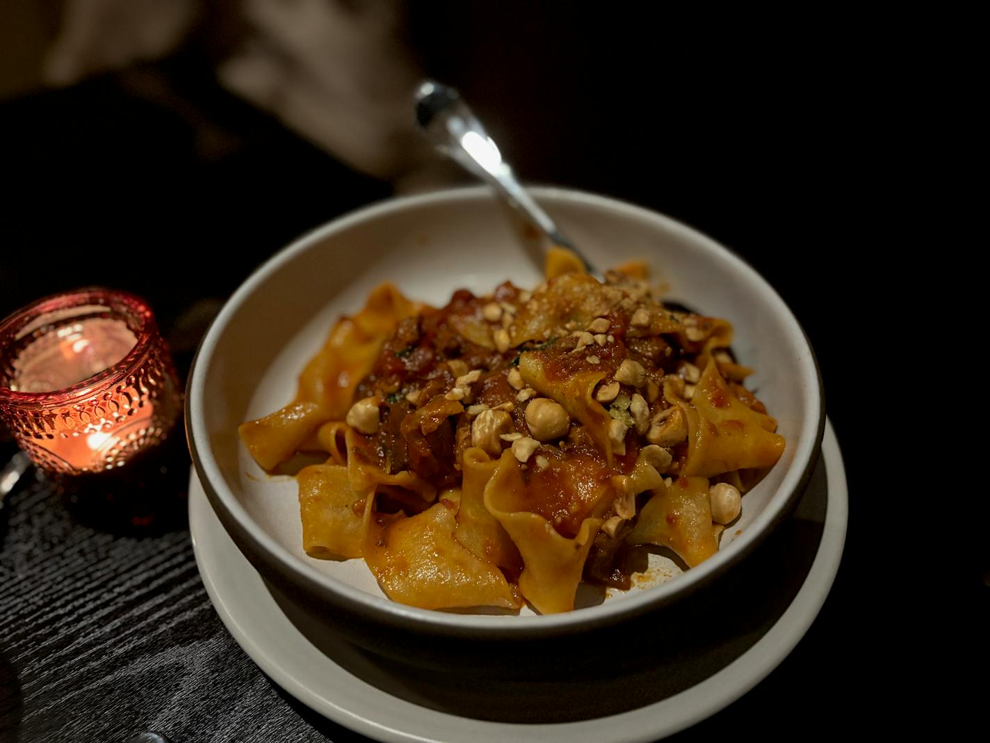 Wide, fresh pasta is served in a bowl with a tomato sauce and hazelnuts.