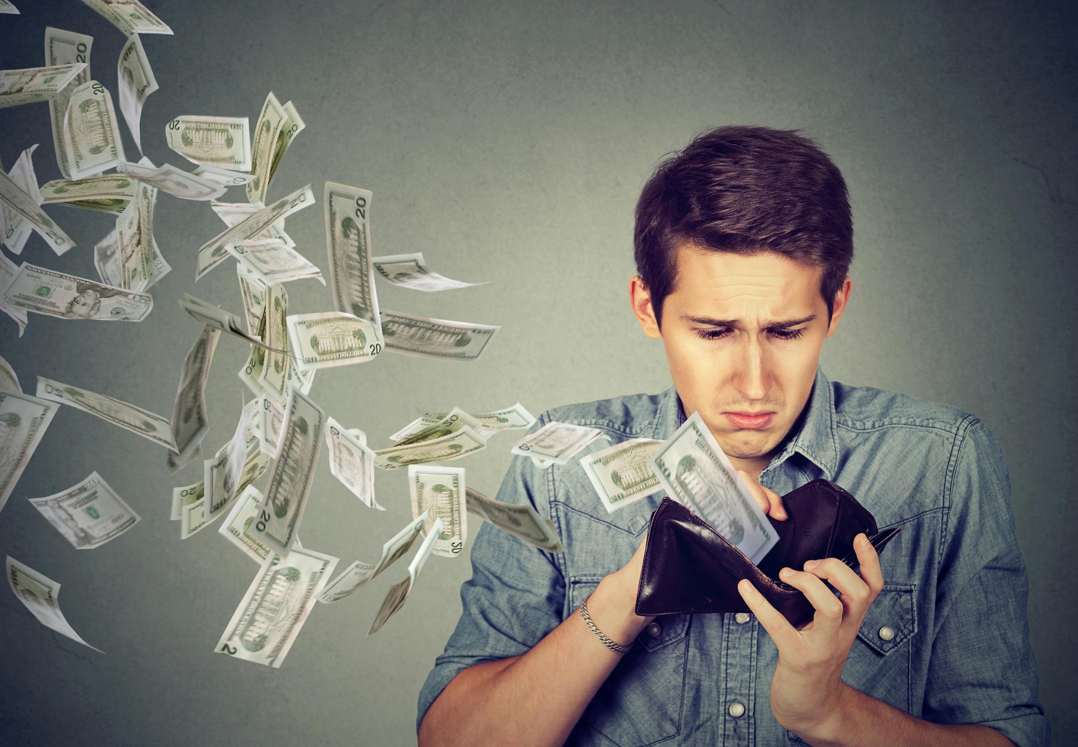 Sad man looking at his wallet with money dollar banknotes flying out away