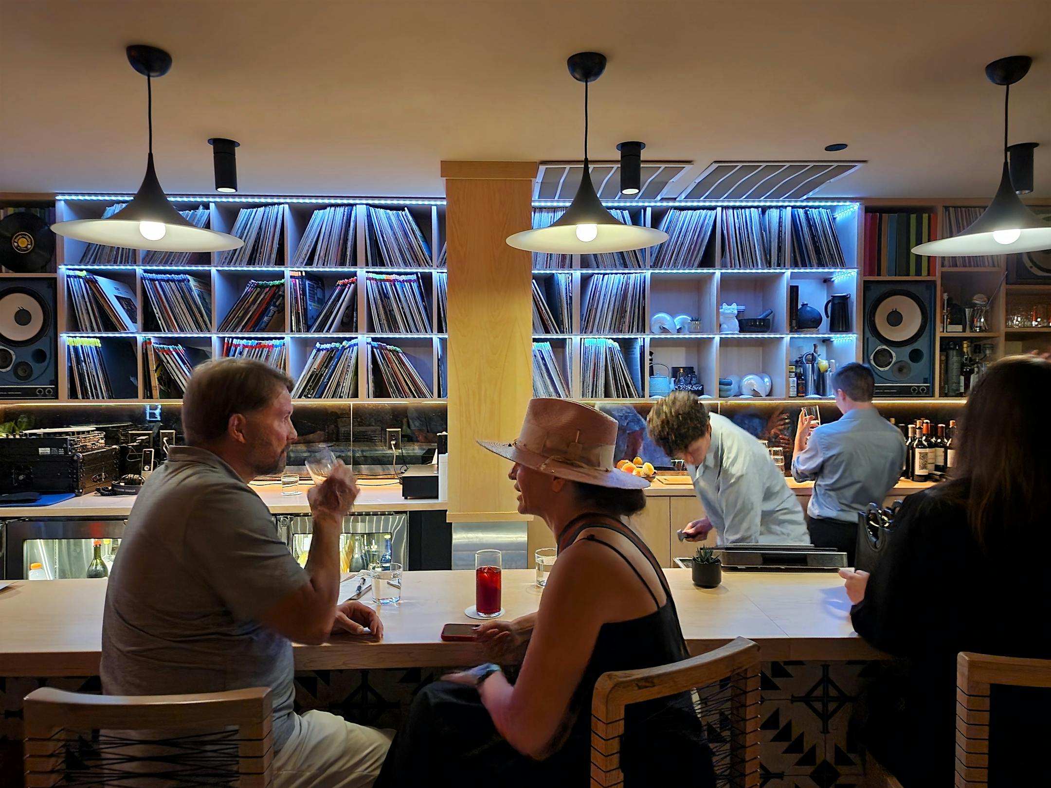 People talking at a bar with shelves of vinyl records behind it.