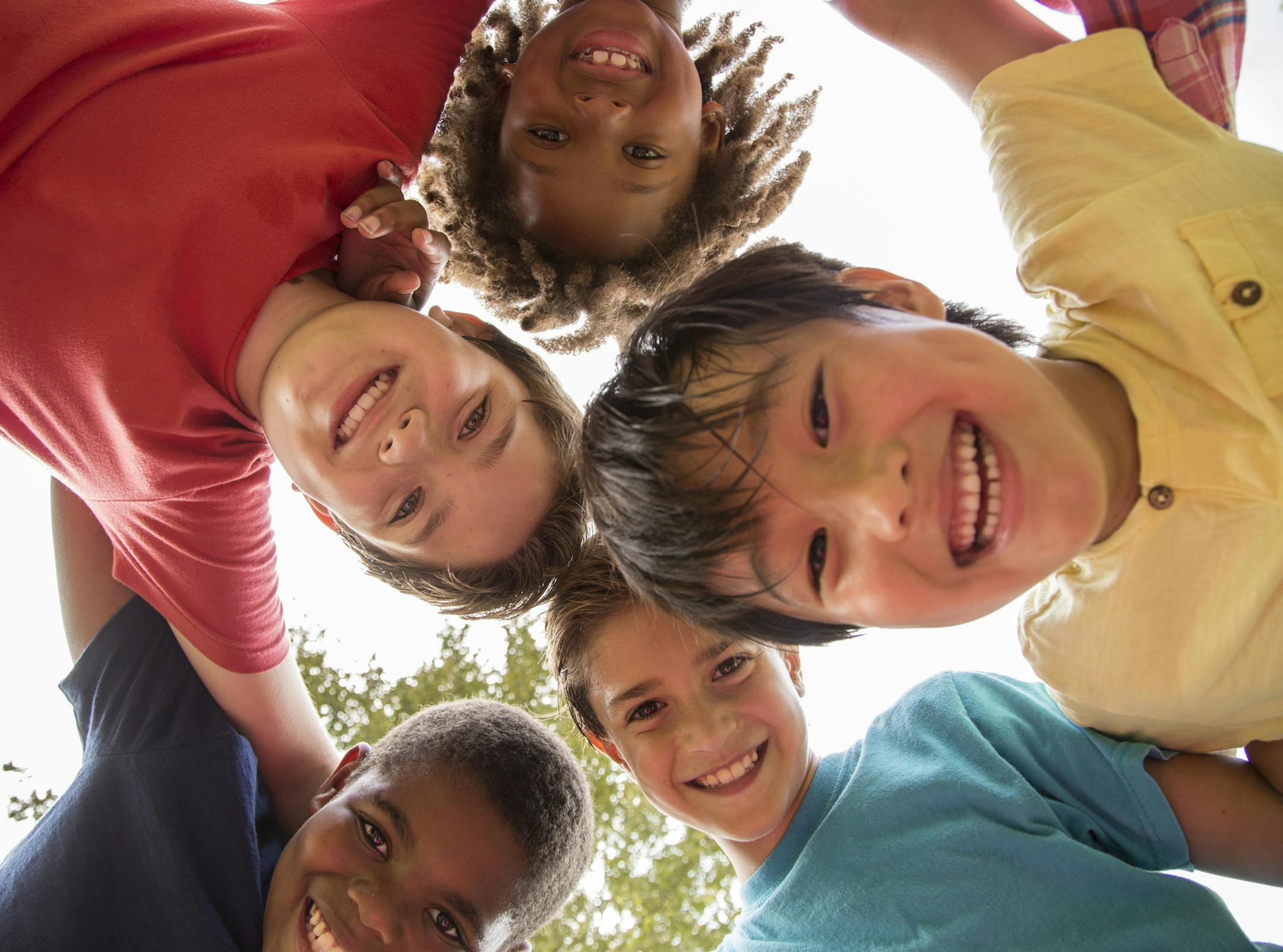Multi-ethnic group of school children playing on school playground. The group of friends huddle up to plan their next adventure. Education in USA, exercise themes. ORG XMIT: 775056179