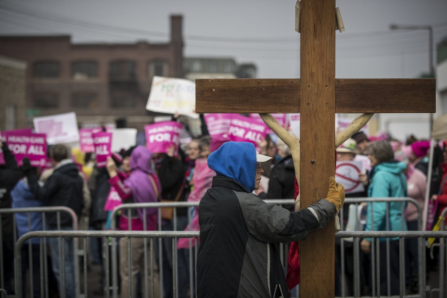 John Janzem held a cross he brought from Sacred Hearts in Robbinsdale as he stood on the pro-life side of a protest outside Planned Parenthood in St. Paul, Minn., on April 14, 2017. In the background are pro-choice marchers with signs supporting Planned Parenthood. At this point the vast majority of the pro-life marchers were praying at a cross on the opposite side of the enclosure.