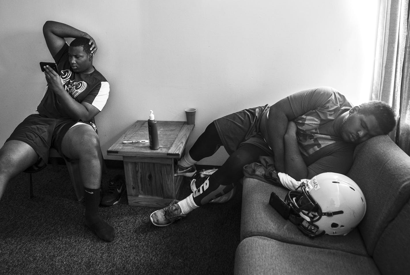 Terrence Allen Sr., of Chicago, left, watched videos on his phone as Uriah "U-U" English, of Louisville, took a brief nap on the couch before a fall camp practice in mid-August. Photos to accompany a story on the Mesabi Range College Football team in Virginia, Minnesota. The team, which consists mostly of black athletes recruited from around the country, struggles to find its place in mostly-white mining country on the Iron Range.