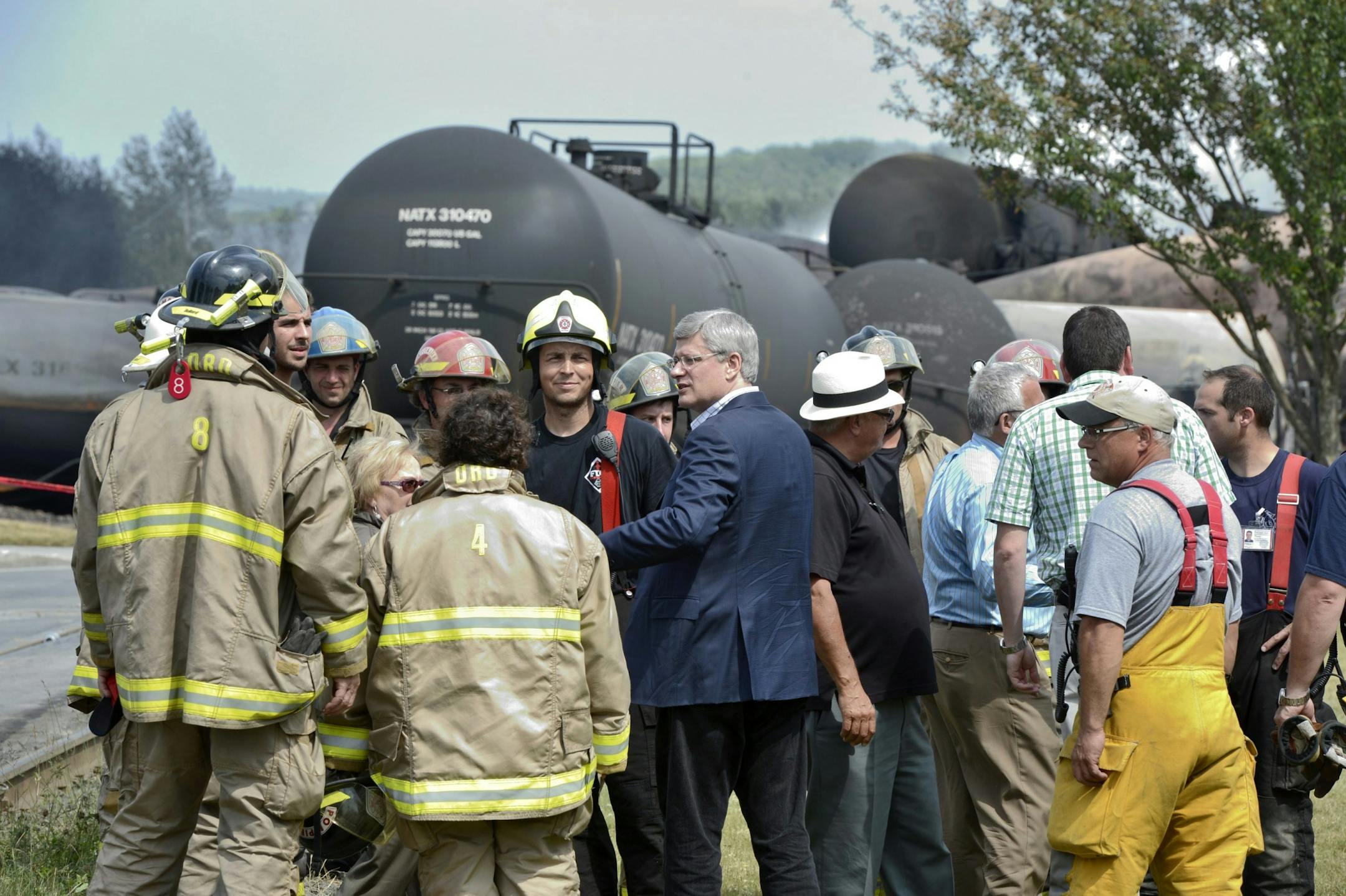 Prime Minister Harper, center, talks with firefighters Sunday, July 7, 2013, in Lac Megantic, Quebec. A runaway train derailed Saturday exploding tanker cars carrying crude oil and destroying part of the downtown area of Lac Megantic.