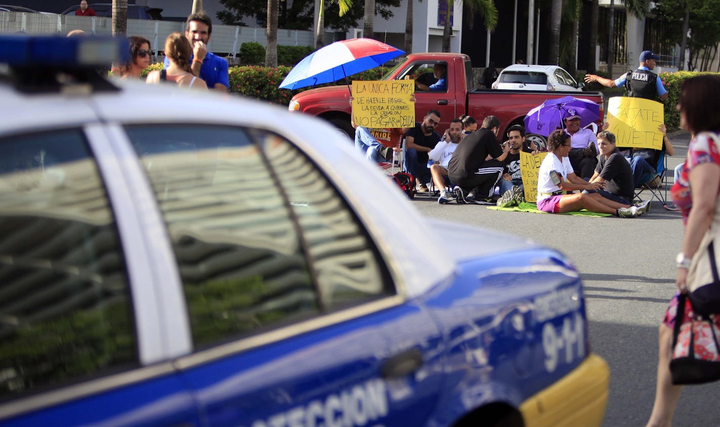 A pedestrian crosses the street as protestors block traffic in the financial district to demand the banking industry take responsibility for the current economic crisis in San Juan, Puerto Rico, Wednesday, July 15, 2015. Protesters gathered along what is known locally as The Golden Mile to demand the island's public debt not be paid back. This month Gov. Alejandro Garcia Padilla said Puerto Rico's outstanding $72 billion public debt is unpayable given the island's long recession. (AP Photo/Ricar