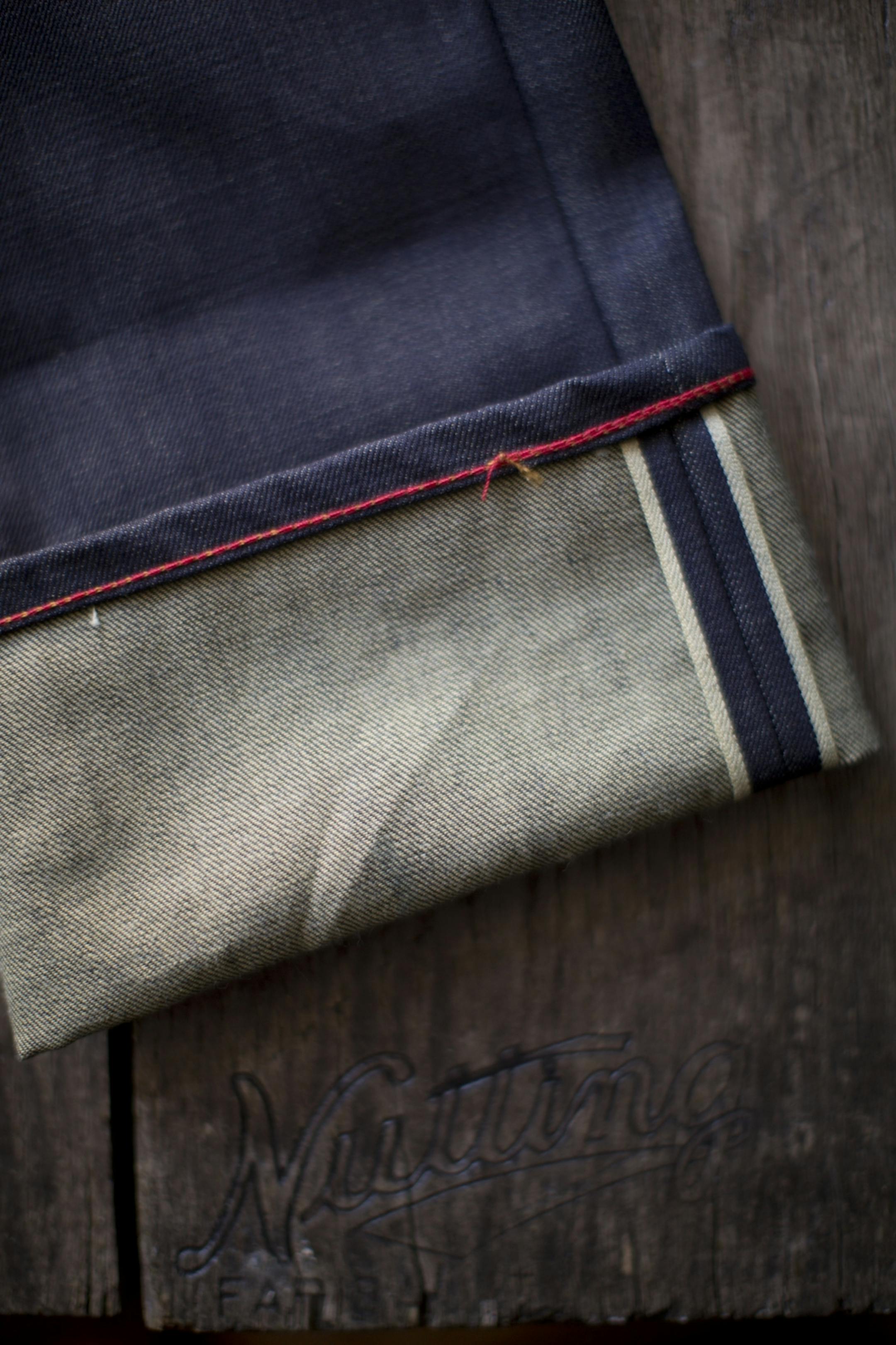 Two indicators of raw denim include the "selvage" (the unfrayed edge of the inseam) and the chainstitching on the hem, which is rare (seen in the red thread at left).