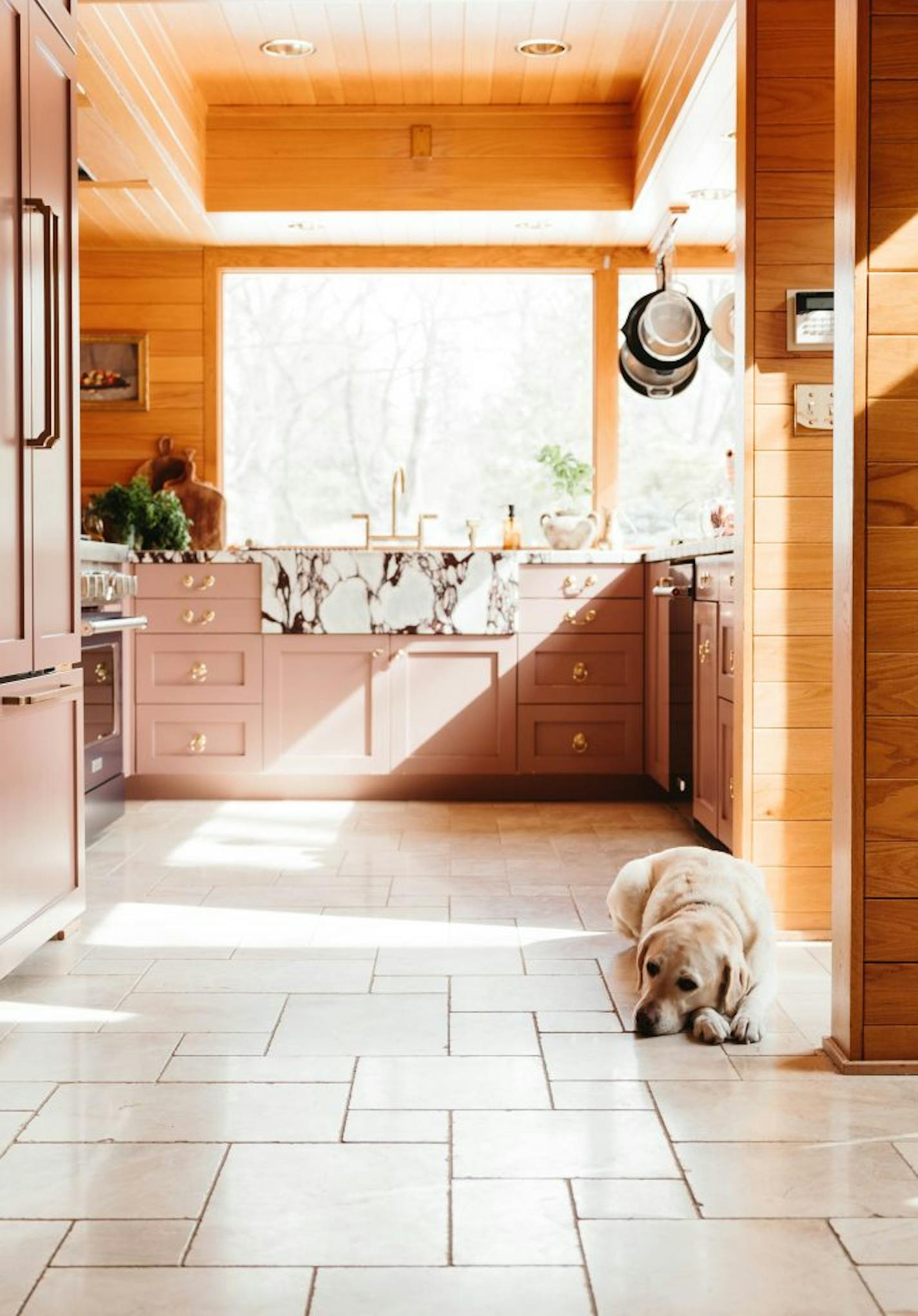 Wit and Delight blogger Kate Arends Peters in her updated St. Paul kitchen with pink cabinetry, a blue range and Calacatta Viola marble countertops that juxtaposes existing red oak paneling.