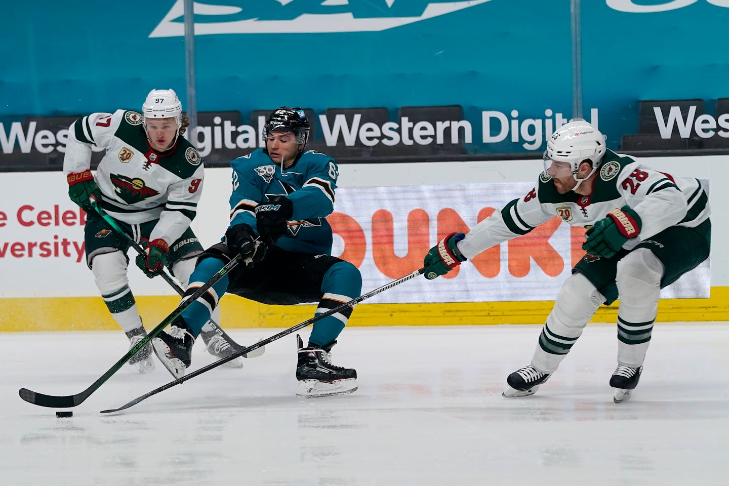 San Jose Sharks right wing Kevin Labanc, middle, reaches for the puck between Minnesota Wild left wing Kirill Kaprizov (97) and defenseman Ian Cole (28) during the first period of an NHL hockey game in San Jose, Calif., Wednesday, March 31, 2021. (AP Photo/Jeff Chiu)