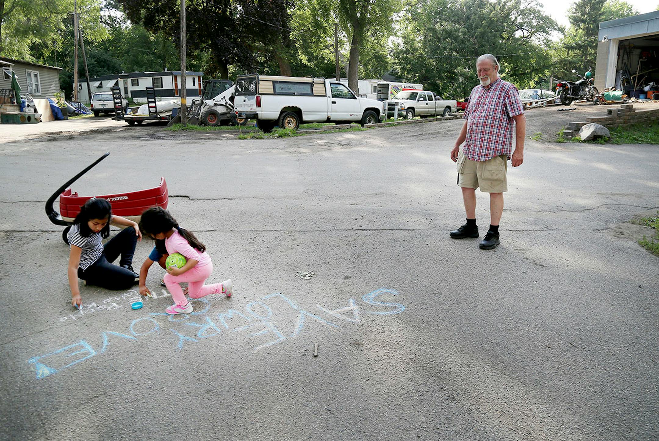 Lowry Grove mobile home park resident Bill McConnell, a retiree who has lived at Lowry Grove for 31 years, watches as children chalk the road with a message to save the park Thursday, June 29, 2017, in St. Anthony, MN. "This is where I was going to retire," McConnell said. Lowry Grove closed it's gate and all residents had to be gone by 12 midnight on July 1, the space slated to be redeveloped into multiple-family housing.