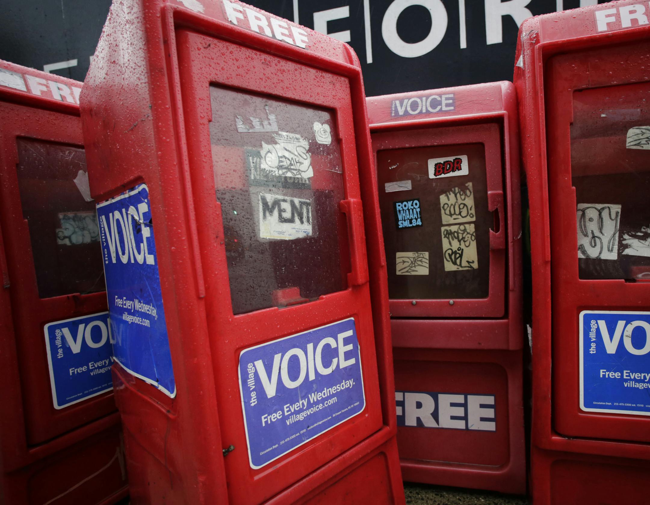 In this Nov. 27, 2013 photo, plastic newspaper boxes for The Village Voice stand along a Manhattan sidewalk in New York. Village Voice publisher Peter Barbey announced on Friday, Aug. 31, 2018, that the venerable alternative weekly will cease publication. The announcement comes three years after Barbey bought the paper and one year after it ceased publishing in print. (AP Photo/Mark Lennihan)