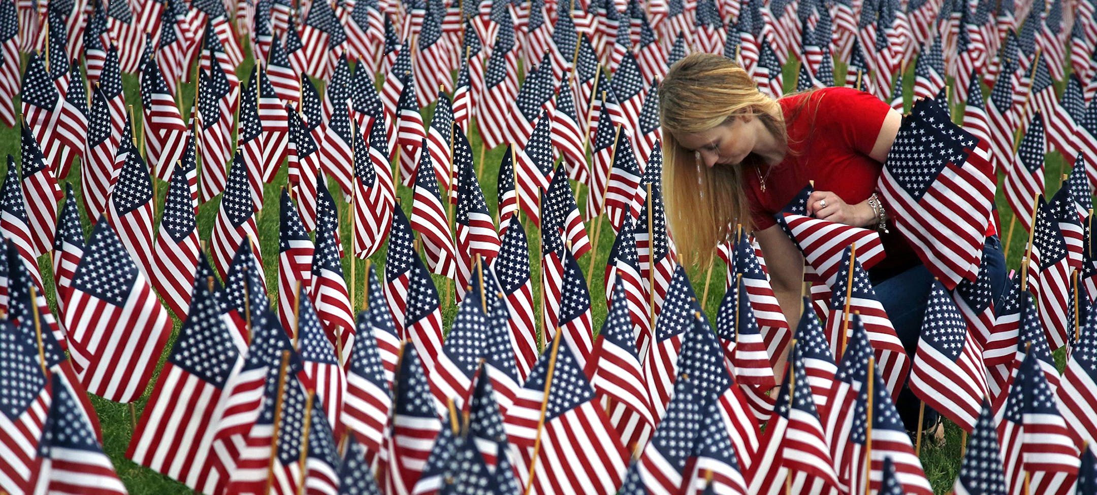 Volunteer Shannon Day of Boston helps to plant some of the 37,000 flags at the Boston Common, Wednesday, May 22, 2014, in memory of every fallen service member from the Revolutionary War to the present. The flags will be on display throughout Memorial Day weekend. (AP Photo/Elise Amendola) ORG XMIT: MIN2014052218372266