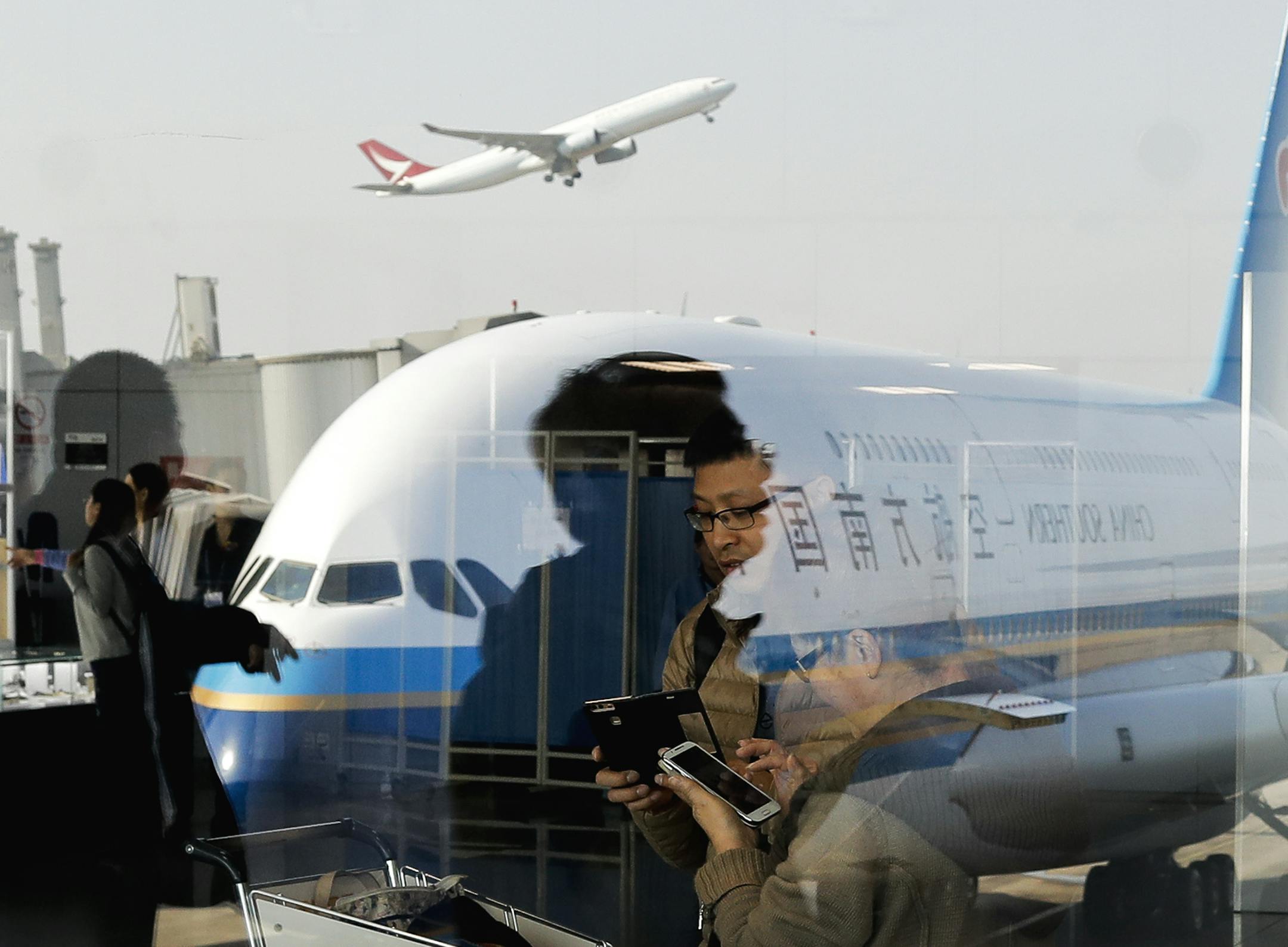 Passengers walk past a couple browsing their smartphones near an Airbus A380 passenger airplane, owned by China Southern Airlines, parked on the tarmac at the Beijing Capital International Airport Saturday, Nov. 19, 2016. China's President Xi Jinping made an impassioned call against protectionism at a summit of Asian-Pacific leaders as Chinese state media blasted U.S. President-elect Donald Trump for trade-bashing it says could drag the world into "deeper economic distress." (AP Photo/Andy Wong)