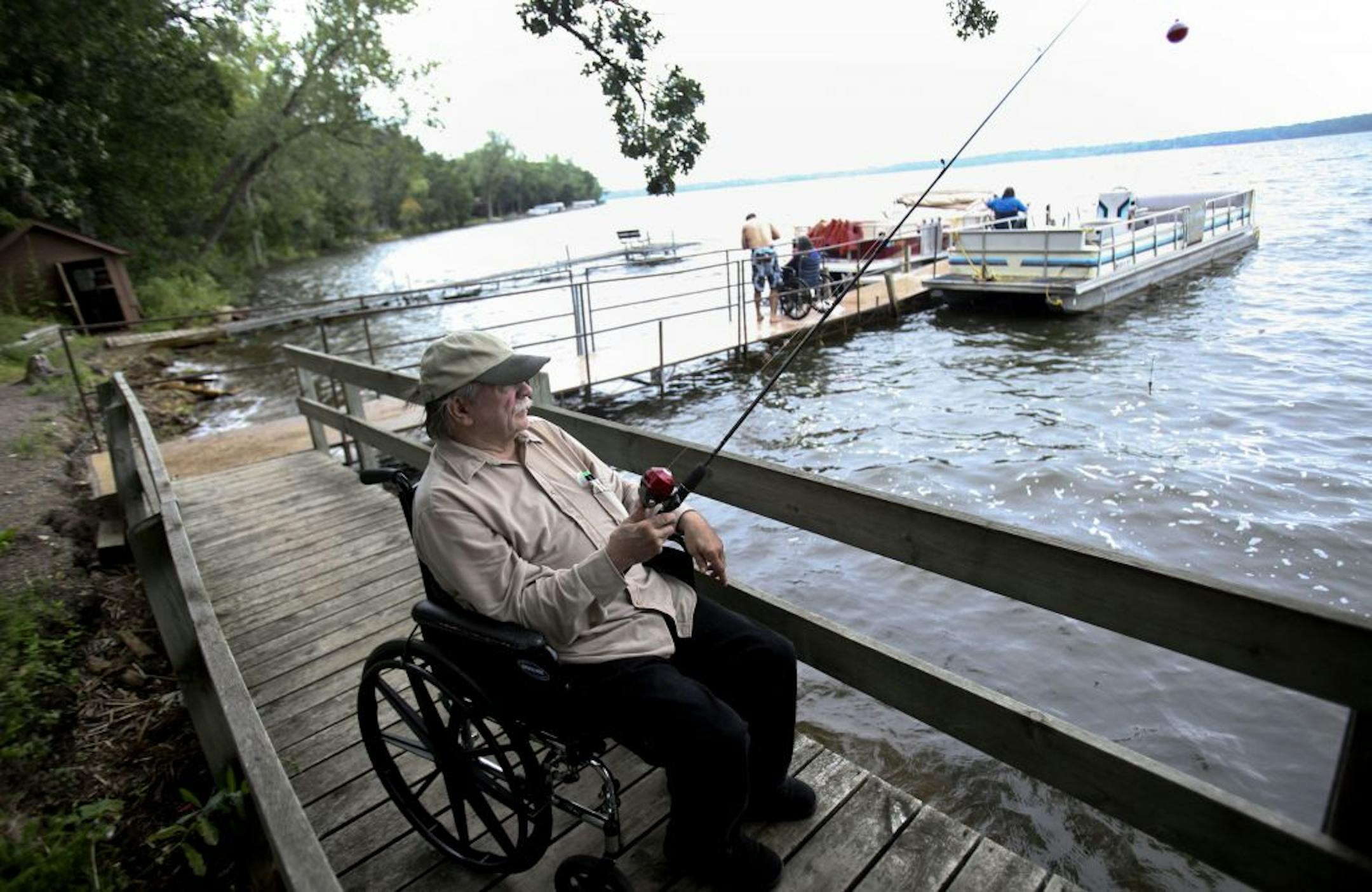 Ed Erickson, resident of Camden Care Center nursing home, tried to stay out of the rain has he fished off the dock along with other residents who enjoyed an afternoon of fishing at Camp Friendship in Annandale, Minn., Tuesday, August 16, 2011. More than 40 residents signed up for this overnight getaway up to Clearwater Lake.