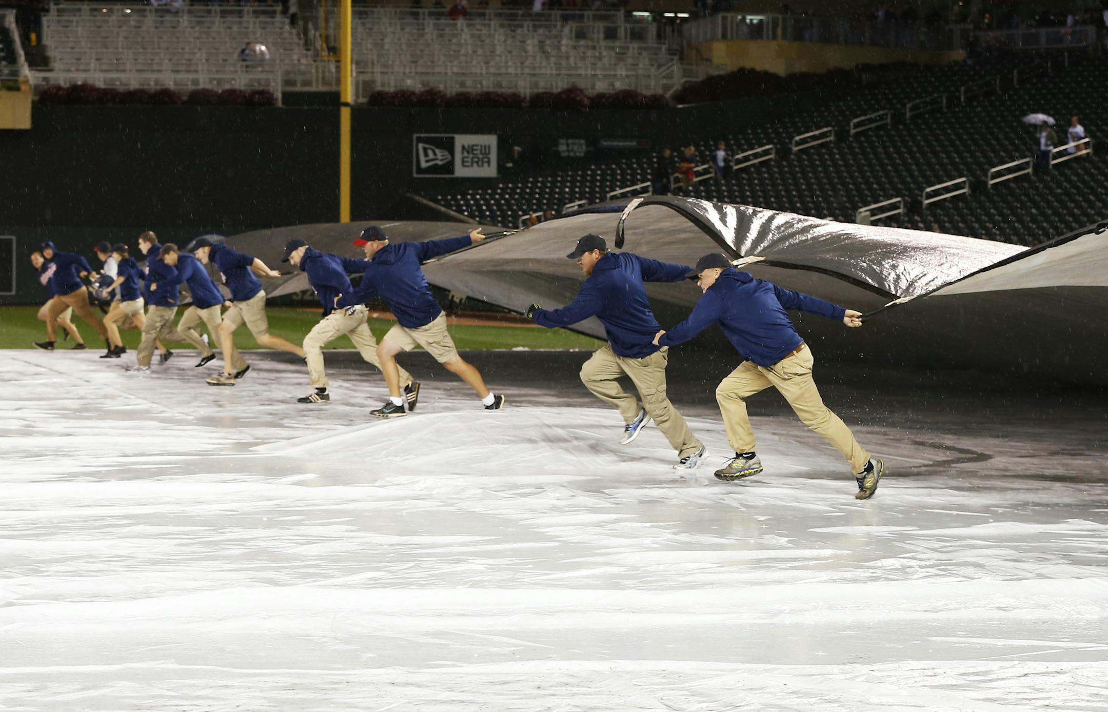 Minnesota Twins grounds crew members empty standing water from the field tarp after a baseball game against the against the Los Angeles Angels was postponed due to rain, Friday, Sept. 18, 2015, in Minneapolis. The game will be made up as part of a split double header Saturday. (AP Photo/Jim Mone)