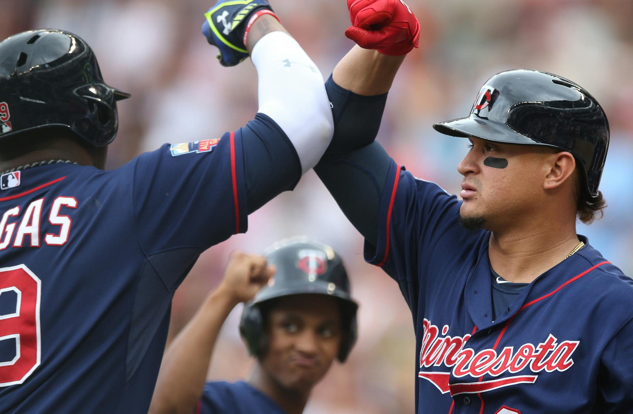 Minnesota Twins' Oswaldo Arcia, right, gives an elbow bump to Kennys Vargas as a ball boy, center, waits his turn after Vargas hit a solo home run off Cleveland Indians pitcher Corey Kluber in the fourth inning of a baseball game, Thursday, Aug. 21, 2014, in Minneapolis. (AP Photo/Jim Mone)