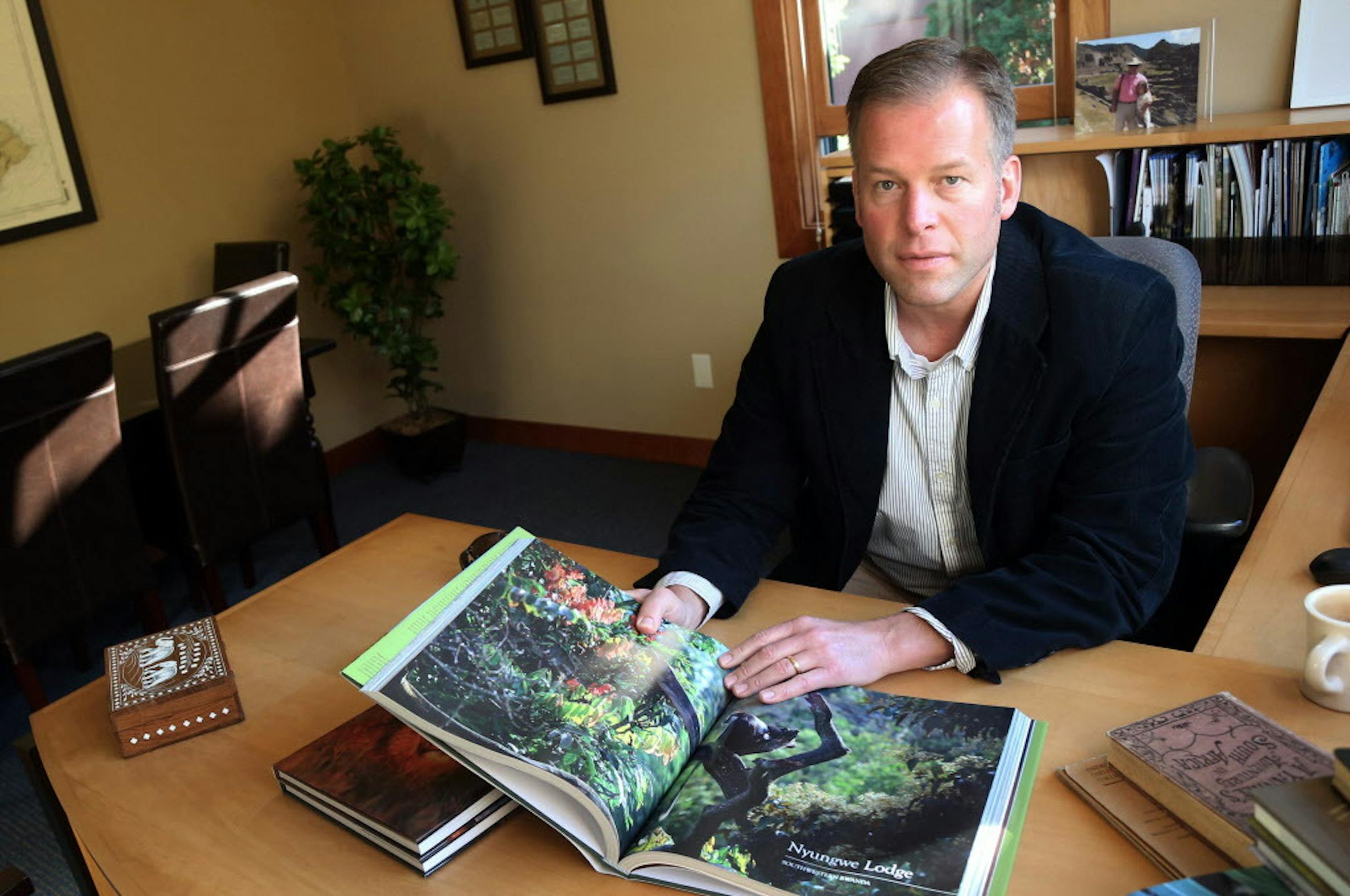 In this Oct. 21, 2014 photo, Craig Beal, owner of Travel Beyond, poses with books on Africa at his travel agency in Wayzata, Minn. Fear about the Ebola virus spreading is hurting businesses like Beal's. He has had three cancellations for safaris to places like Botswana and South Africa that are nine hours by plane from the countries with widespread outbreaks. (AP Photo/Jim Mone)