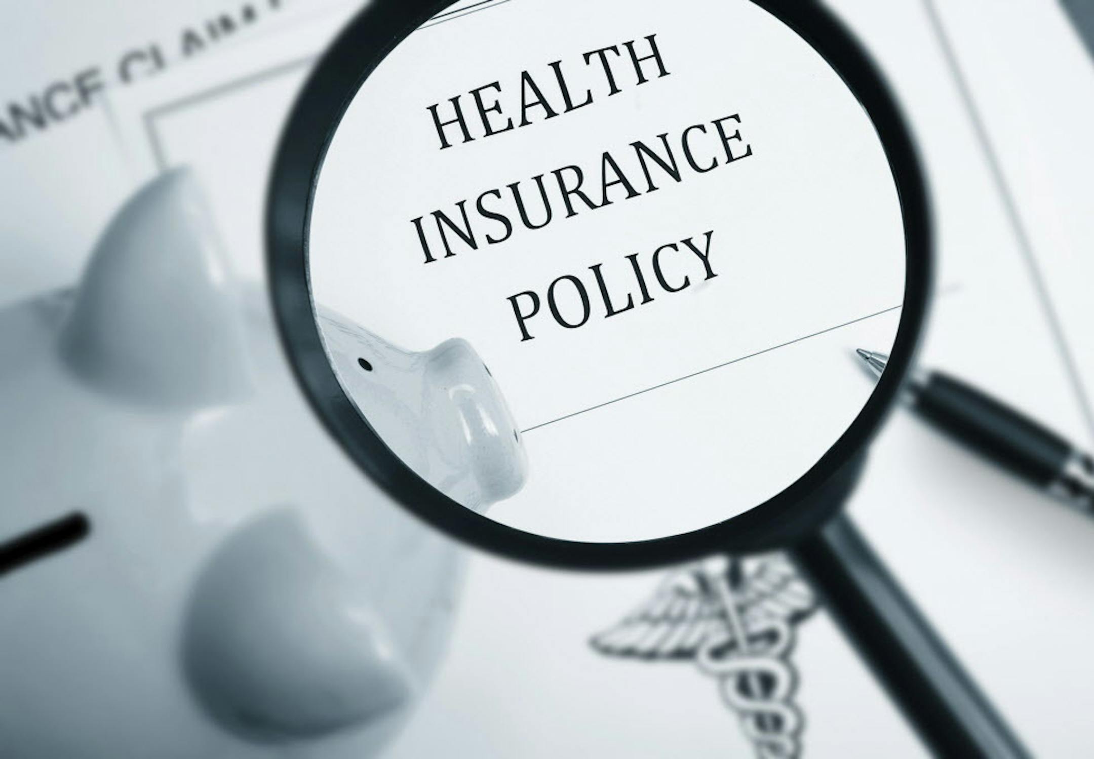 Magnifying glass over health insurance policy and piggy bank