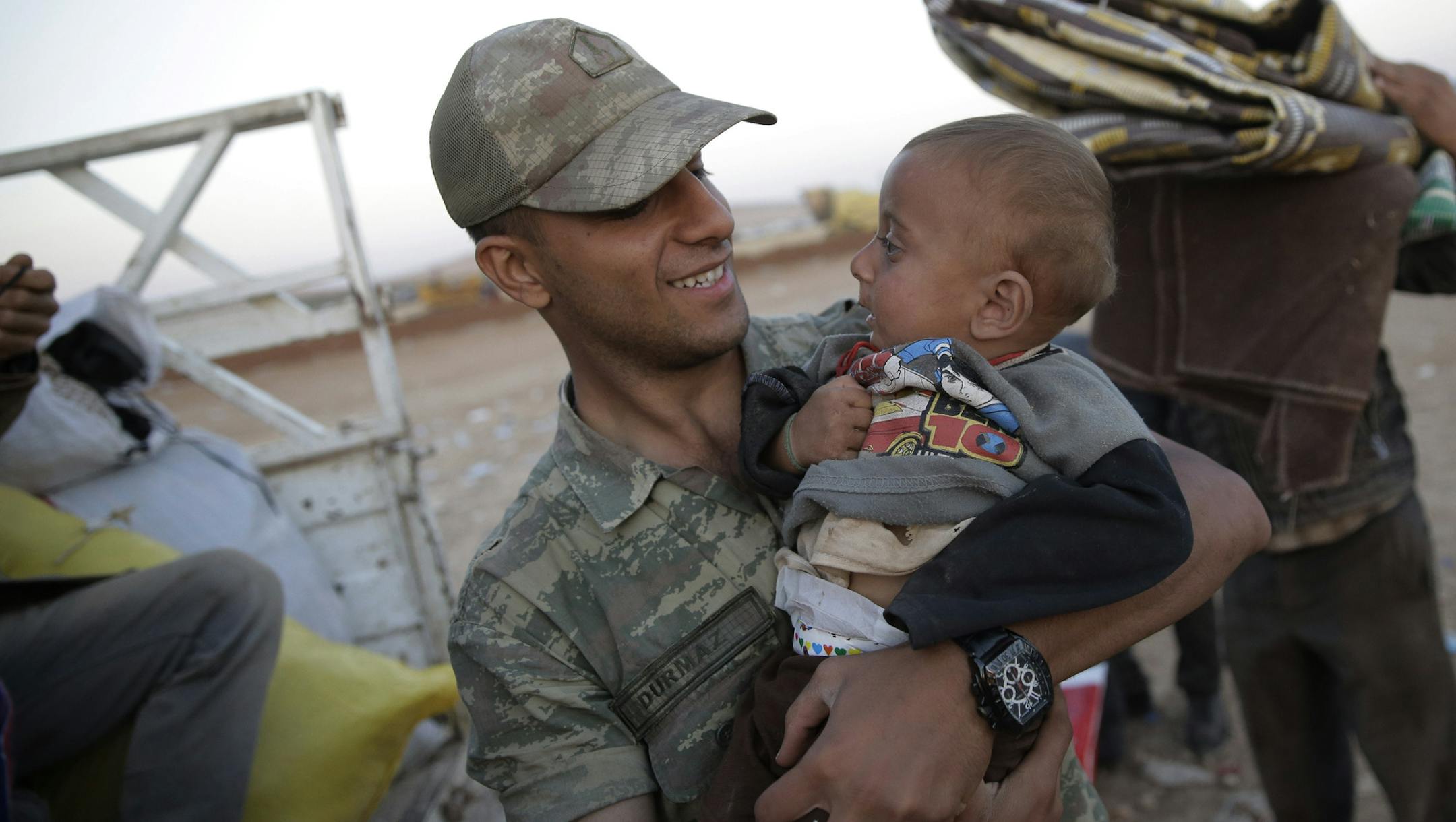 A Turkish soldier carries a young Syrian Kurdish refugee to board a truck near Suruc, Turkey, after the family's arrival from Kobani, as fighting intensified between Syrian Kurds and the militants of Islamic State group, Sunday, Oct. 5, 2014. Kobani, also known as Ayn Arab, is just a few hundred meters inside Syria and its surrounding areas have been under attack since mid-September, with militants capturing dozens of nearby Kurdish villages. (AP Photo/Lefteris Pitarakis)