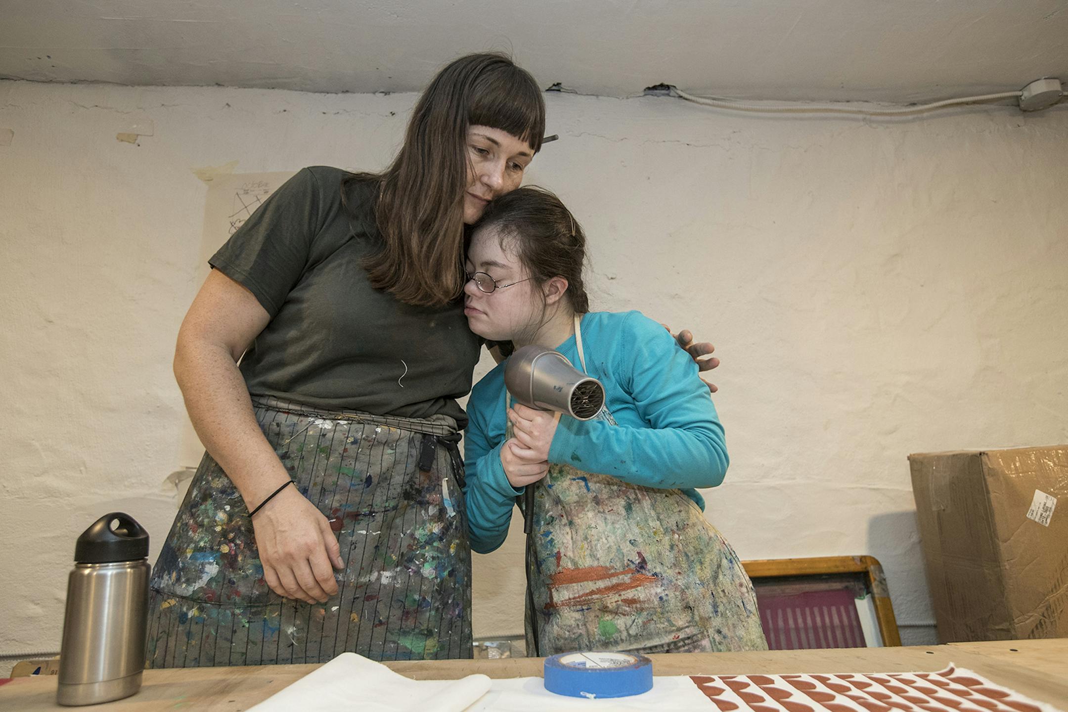 Julia Tyler, right, leans in for a little hug from her job coach, Liv Helgesen, left. Liv and Julia have been together for four years and they work on Julia's silk screening company, Dance Happy Designs, three days a week in the basement of the Compendium Boutique. (Michael Bryant/Philadelphia Inquirer/TNS) ORG XMIT: 1540254 ORG XMIT: MIN2001140333081158