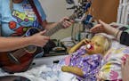 Music therapist Stephanie Epstein, left, stands bedside near Elizabeth "Lizzy" Foley, 2, right, who suffers from Alagille Syndrome, as her mother, Amy