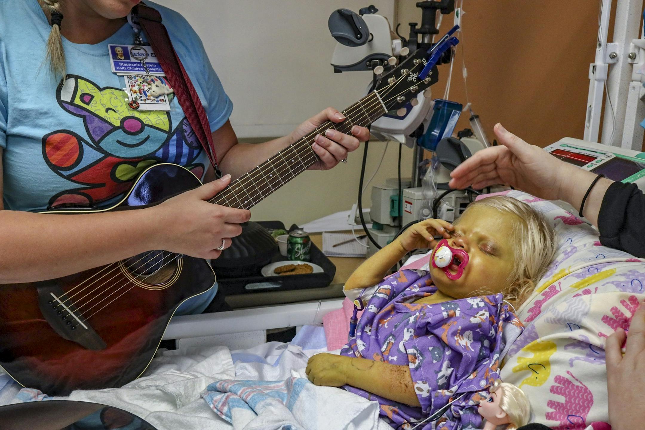 Music therapist Stephanie Epstein, left, stands bedside near Elizabeth "Lizzy" Foley, 2, right, who suffers from Alagille Syndrome, as her mother, Amy Foley, tries to soothe her by stroking her head on Tuesday, October 1, 2019 at the Holtz Children Hospital at UM Jackson Medical Center in Miami, Florida. For the last five years, Stephanie Epstein has soothed the patients at Holtz Children's Hospital with music therapy, a unique way to heal. It also has an added benefit: allowing healthcare provi