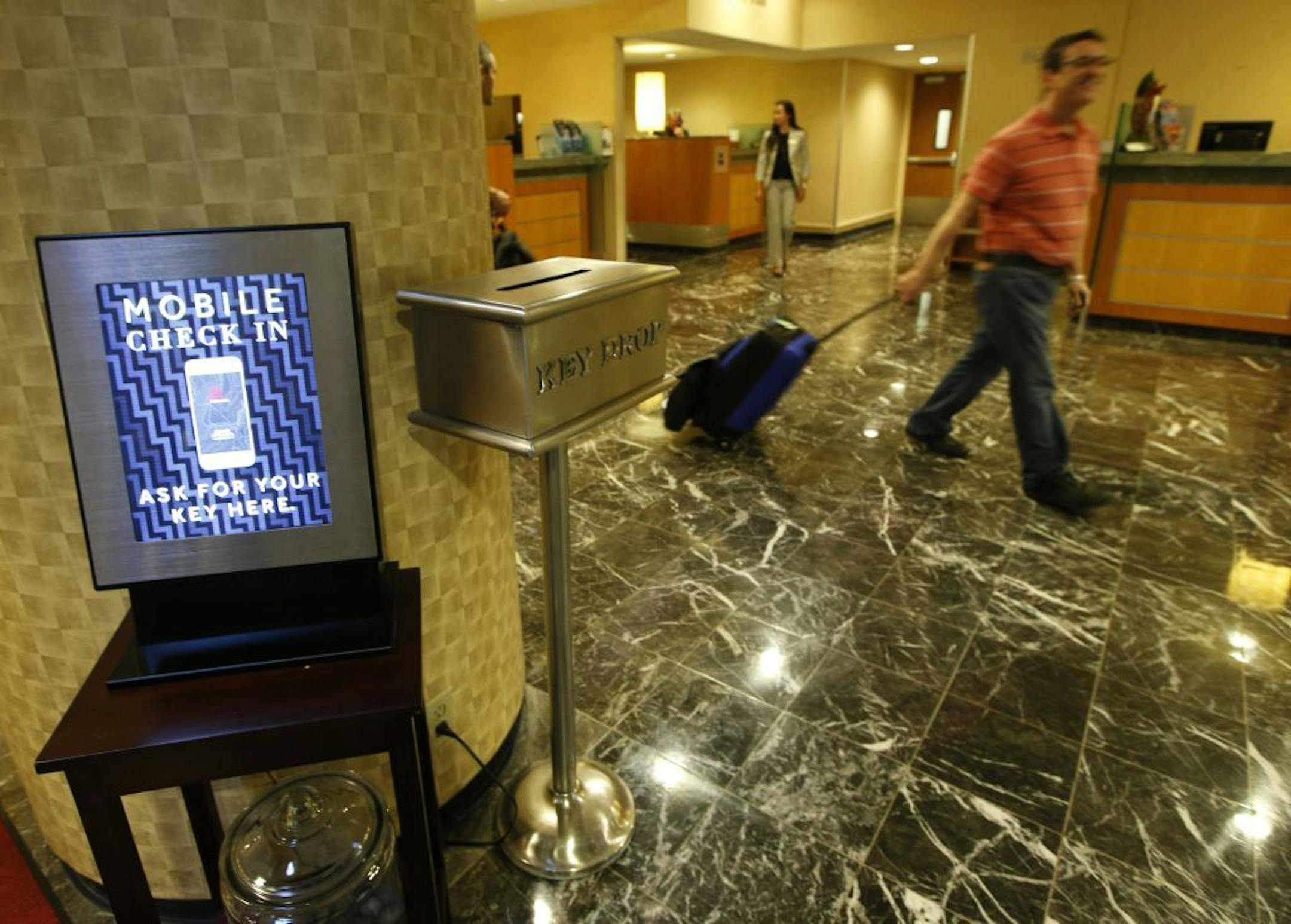 In this Oct. 14, 2014 photo, hotel guest J.D. Solomon, of Indianapolis, right, strolls out of the lobby after using the mobile check-in counter at the Marriott Marquis Times Square hotel in New York. Marriott International launched the ability to check in through its app at 330 North American hotels last year. By the end of this year, the program will be live at all 4,000 hotels worldwide.