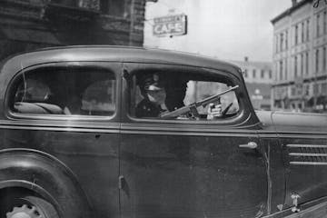 A Ramsey County sheriff’s deputy, armed with a submachine gun, escorts members of the Barker-Karpis gang to court in 1935.  