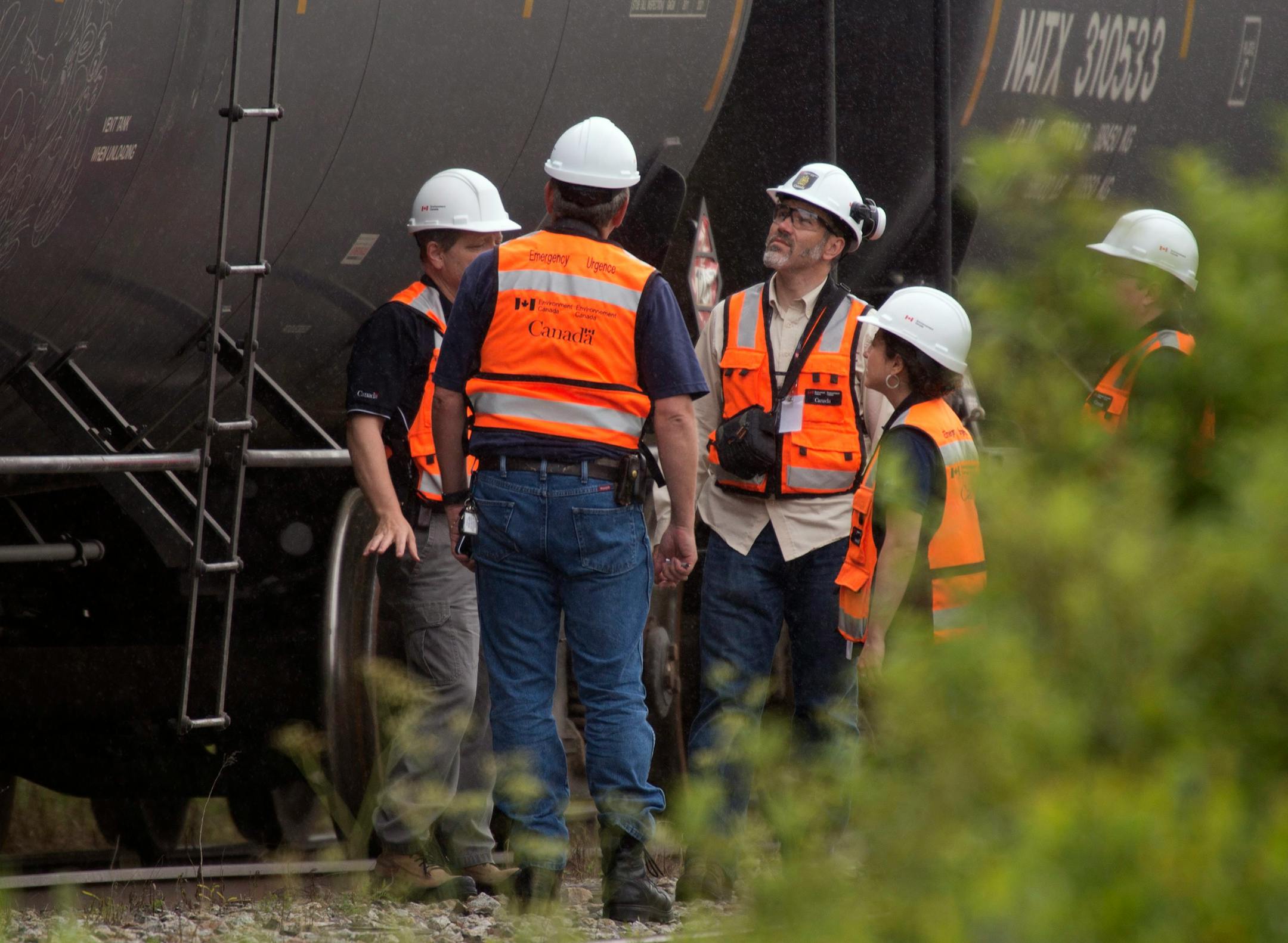 Environment Canada emergency inspectors check on nine MMA tanker cars that remain on the tracks in Nantes, Quebec, Wednesday, July 10, 2013. A train engineer reportedly rushed to borrow a tractor from an area forestry company; grabbed a fireman's suit from an area department; and pushed nine fuel-filled cars weighing 100 tonnes away from the explosive danger on the night of the derailment, according to the company. (AP Photo/The Canadian Press, Jacques Boissinot)