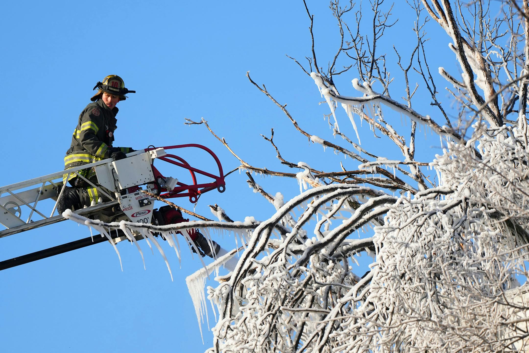 Minneapolis firefighter Toi Yamamoto works from an engine ladder to get more water on hot spots in a building fire near tree frozen from the overspray Saturday, Dec. 3, 2022 in the 2300 block of Lyndale Avenue South in Minneapolis.